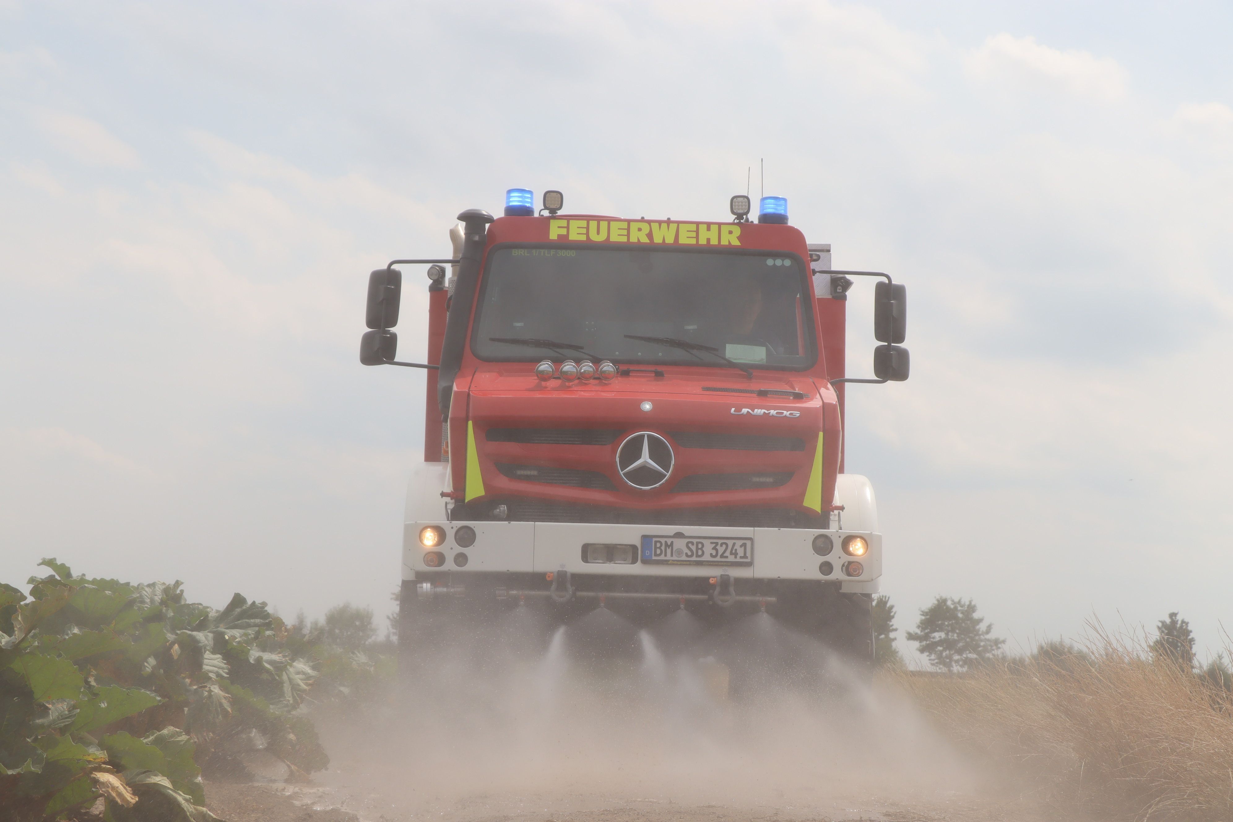 Das Bild zeigt einen Unimog der Feuerwehr Brühl mit eingeschalteten Wasserdüsen.