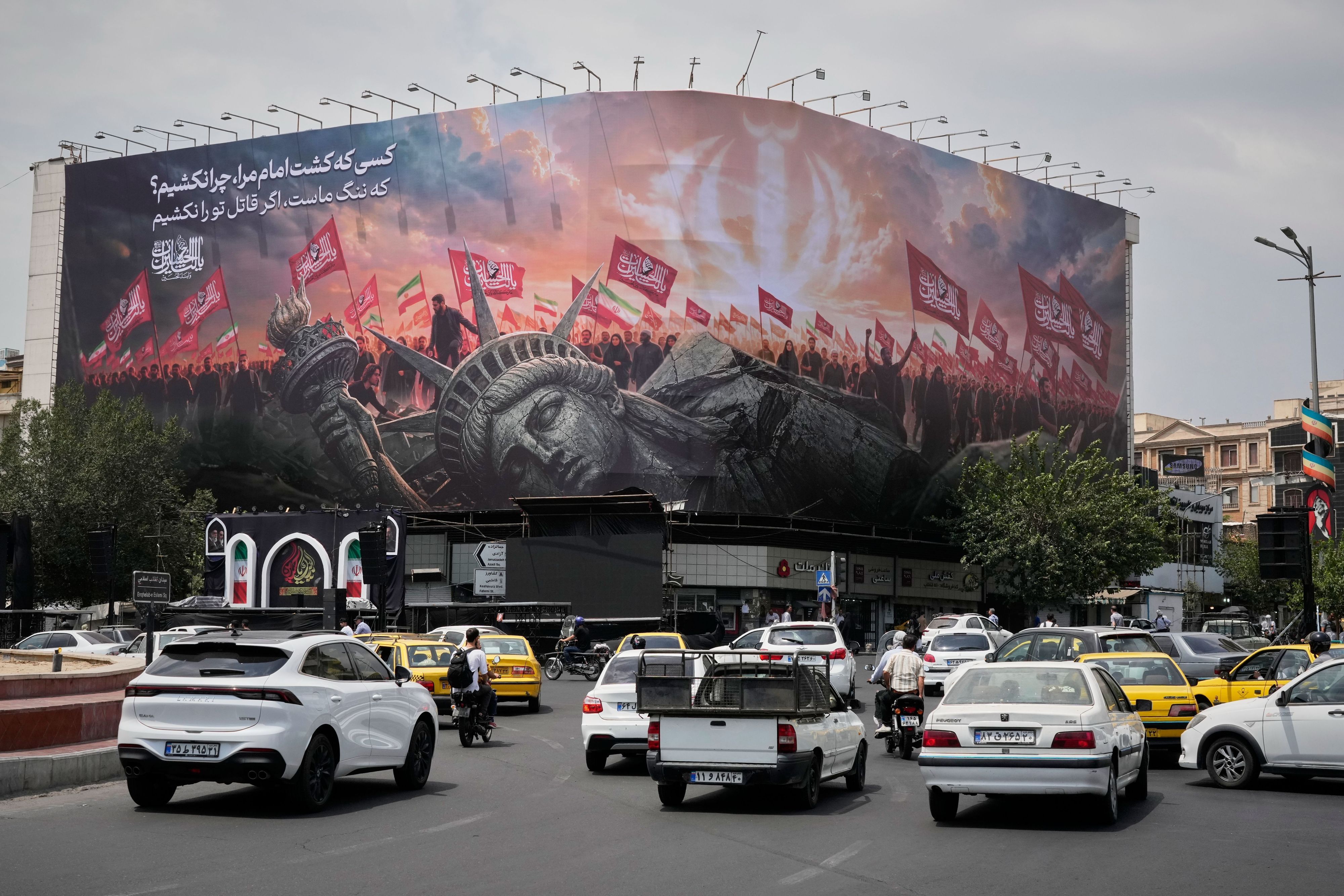 Teheran: Eine Plakatwand, auf der eine umgestürzte Freiheitsstatue und Menschenmengen mit iranischen und schiitischen Flaggen zu sehen sind.