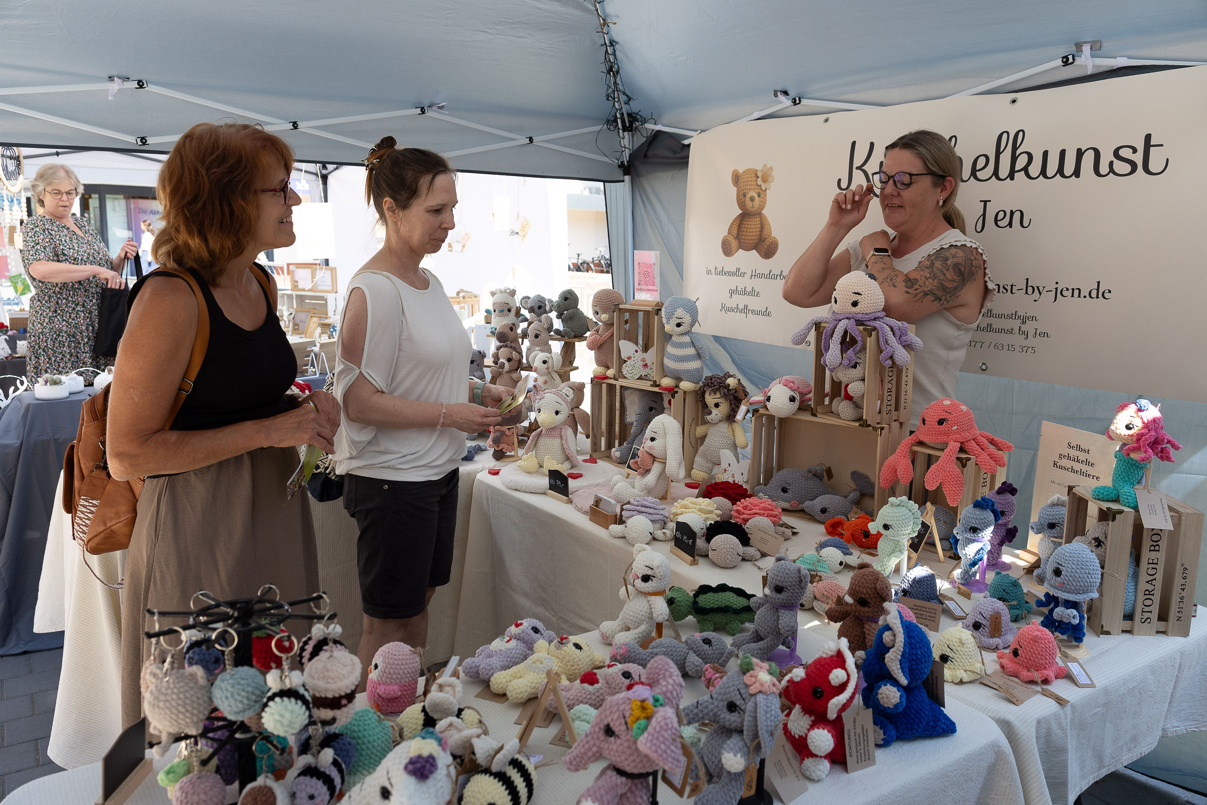 Zwei Besucherinnen schauen sich an einem Stand Amigurumis, gehäkelte Figuren im Mangastil, an.