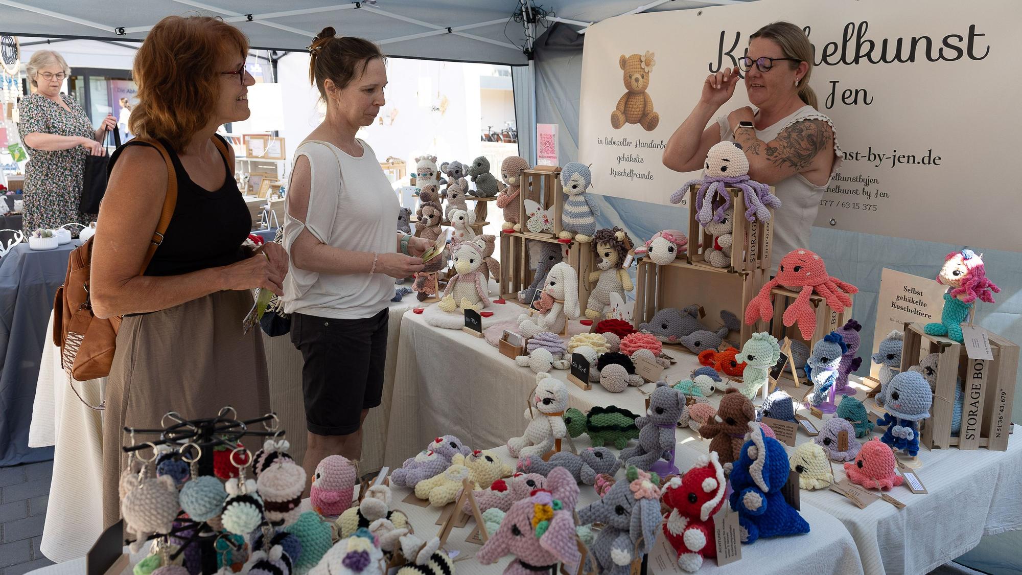 Zwei Besucherinnen schauen sich an einem Stand Amigurumis, gehäkelte Figuren im Mangastil, an.