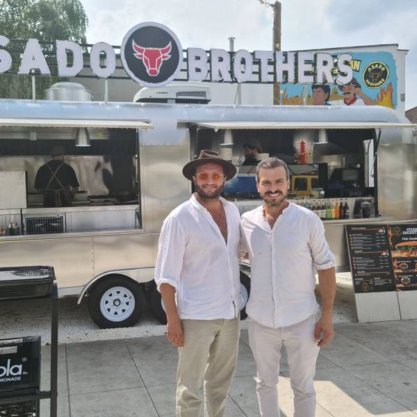 Zwei Männer in weißen Leinenhemden stehen vor einem silbernen Foodtruck.