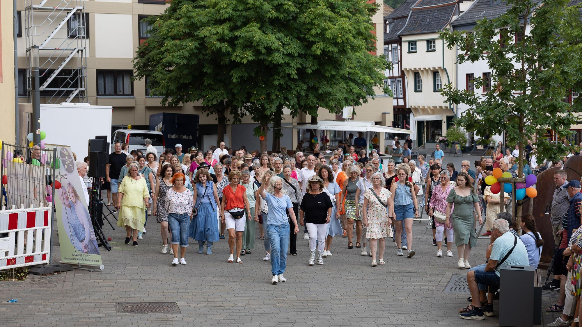Viele Tanzbegeisterte, vornehmlich Frauen, stehen hinter der Tanzlehrerin, die ihren rechten Arm erhoben hat.