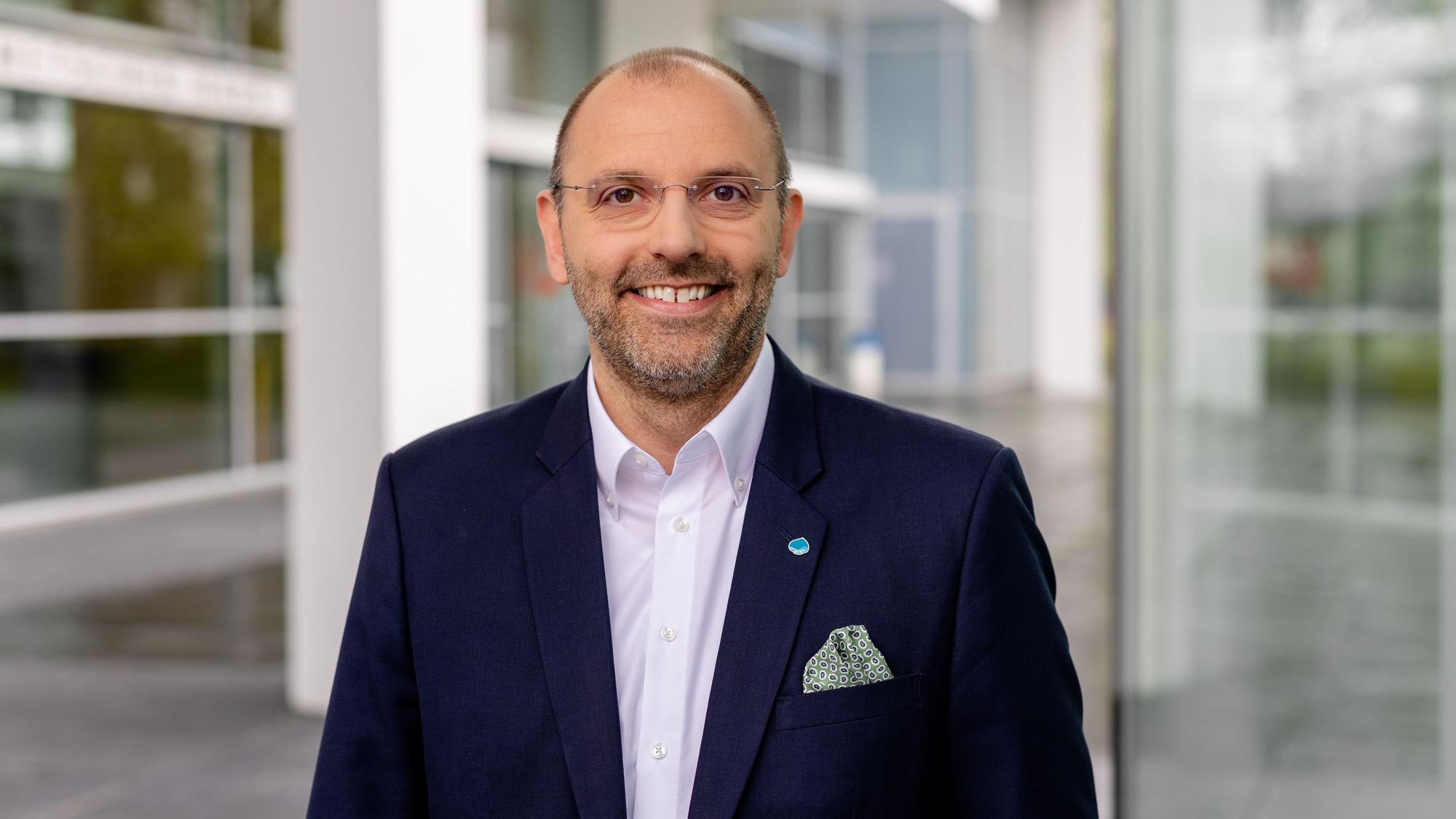 Peter Fintl trägt einen blauen Anzug und blickt lächelnd in die Kamera.