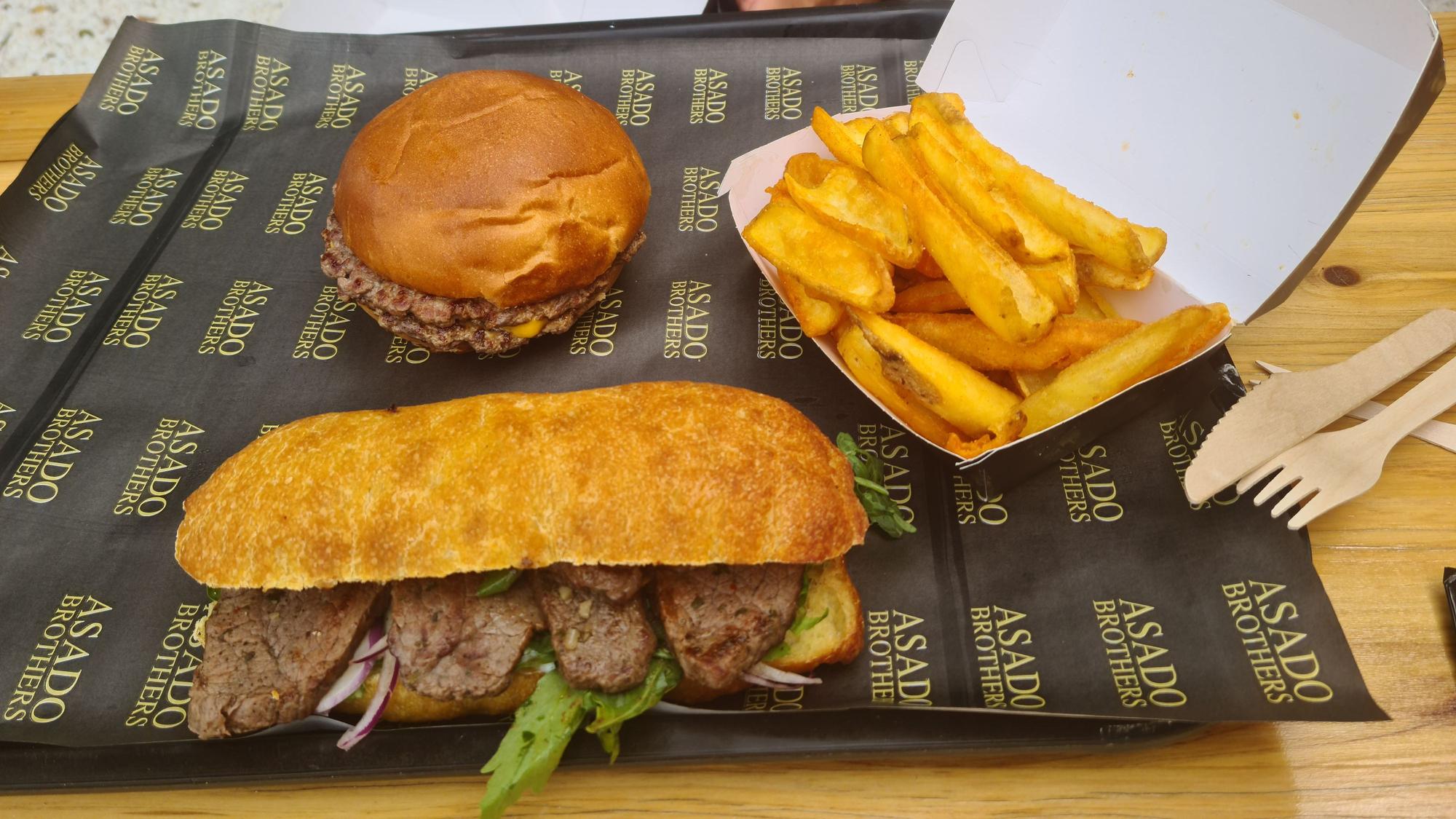Ein Burger, ein Sandwich mit Rindfleisch und eine Portion Fritten liegen verzehrbereit auf einem Tablett.