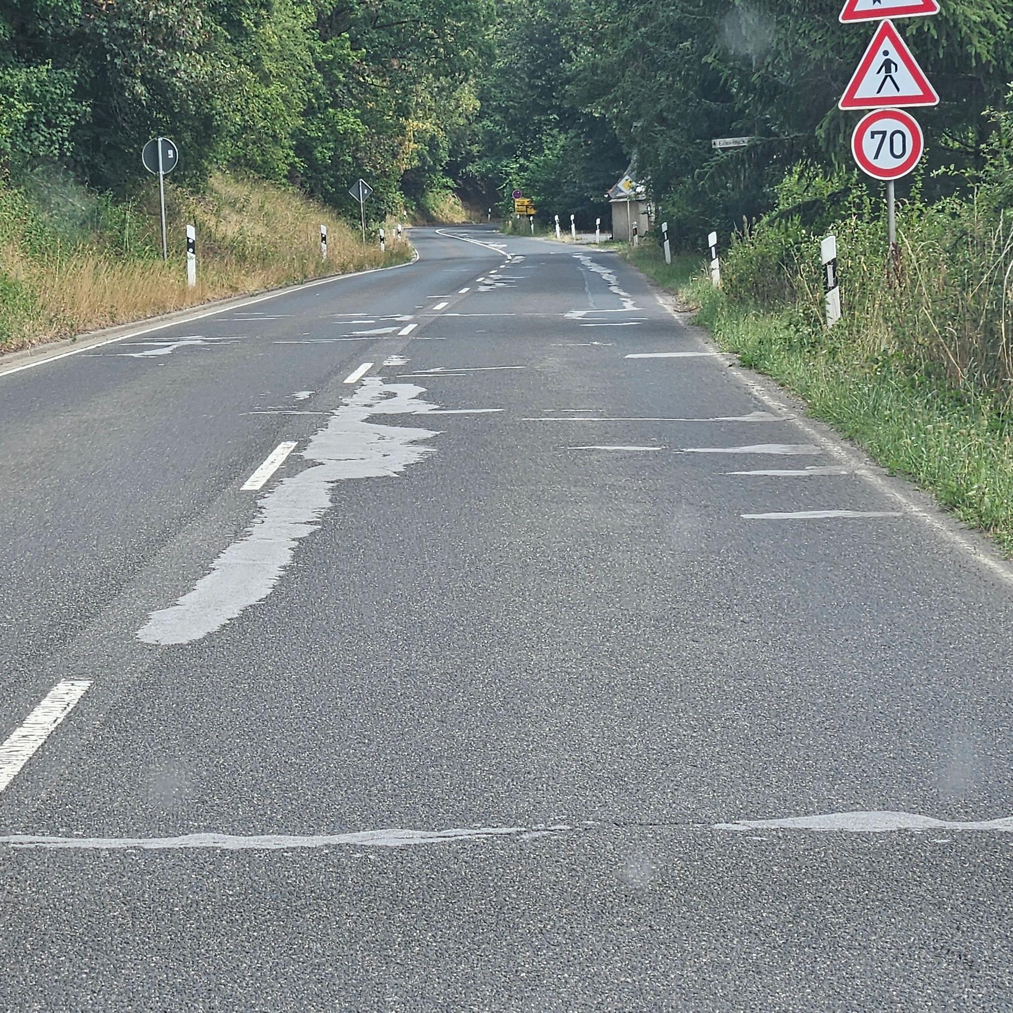 Zu sehen ist eine Straße mit mehreren hellen Ausbesserungsstellen.