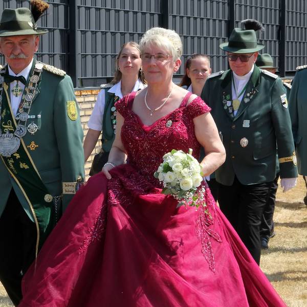 Männer und Frauen in Schützenuniformen und eine Frau in rotem Kleid gehen durch einen Ort.