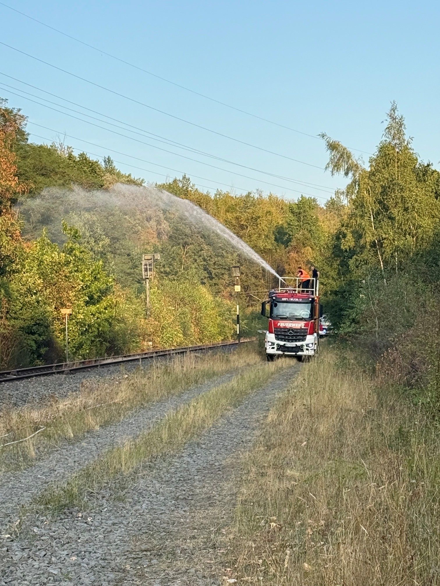 Das Bild zeigt ein Feuerwehrfahrzeug auf einem Weg parallel zu Bahngleisen.
