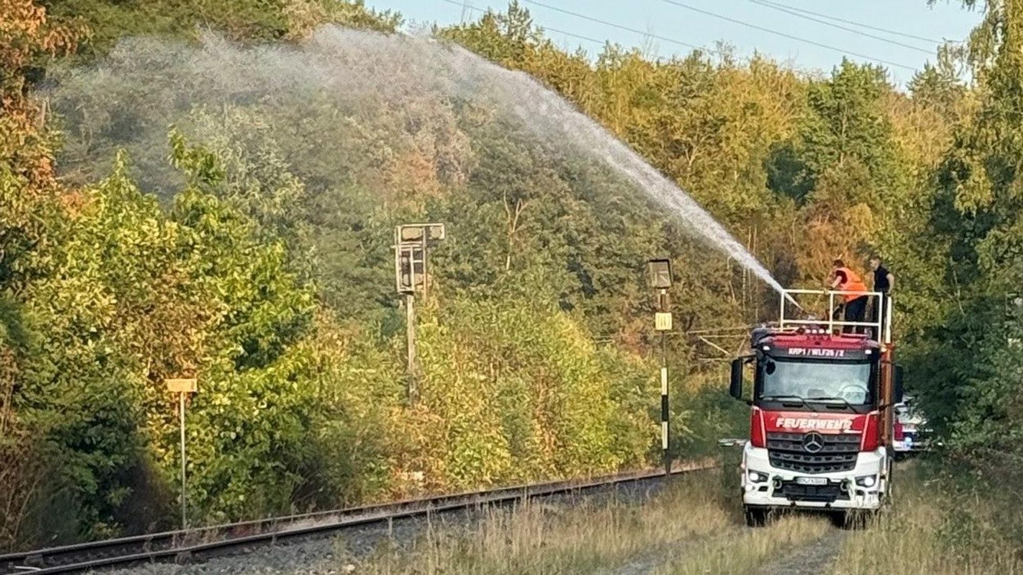 Das Bild zeigt ein Feuerwehrfahrzeug auf einem Weg parallel zu Bahngleisen.