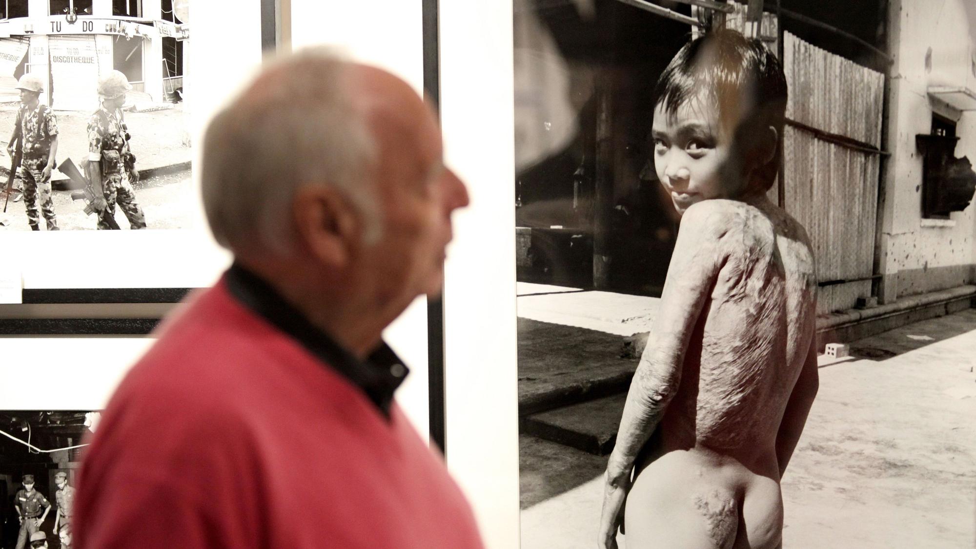 Der Kriegsfotograf Perry Kretz steht bei der Ausstellung „Augen auf und durch!“ im Stadtmuseum Schleswig neben dem berühmten Foto von Kim Phuc, das die damals neunjährige Vietnamesin nach dem Napalm-Angriff im Vietnamkrieg zeigt.