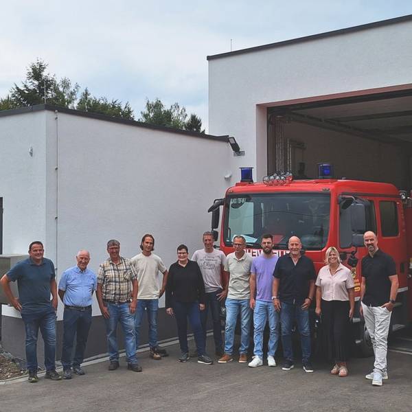 Die Genannten haben sich zum Gruppenbild vor der Wagenhalle mit dem Löschfahrzeug und dem Gerätehaus aufgestellt.