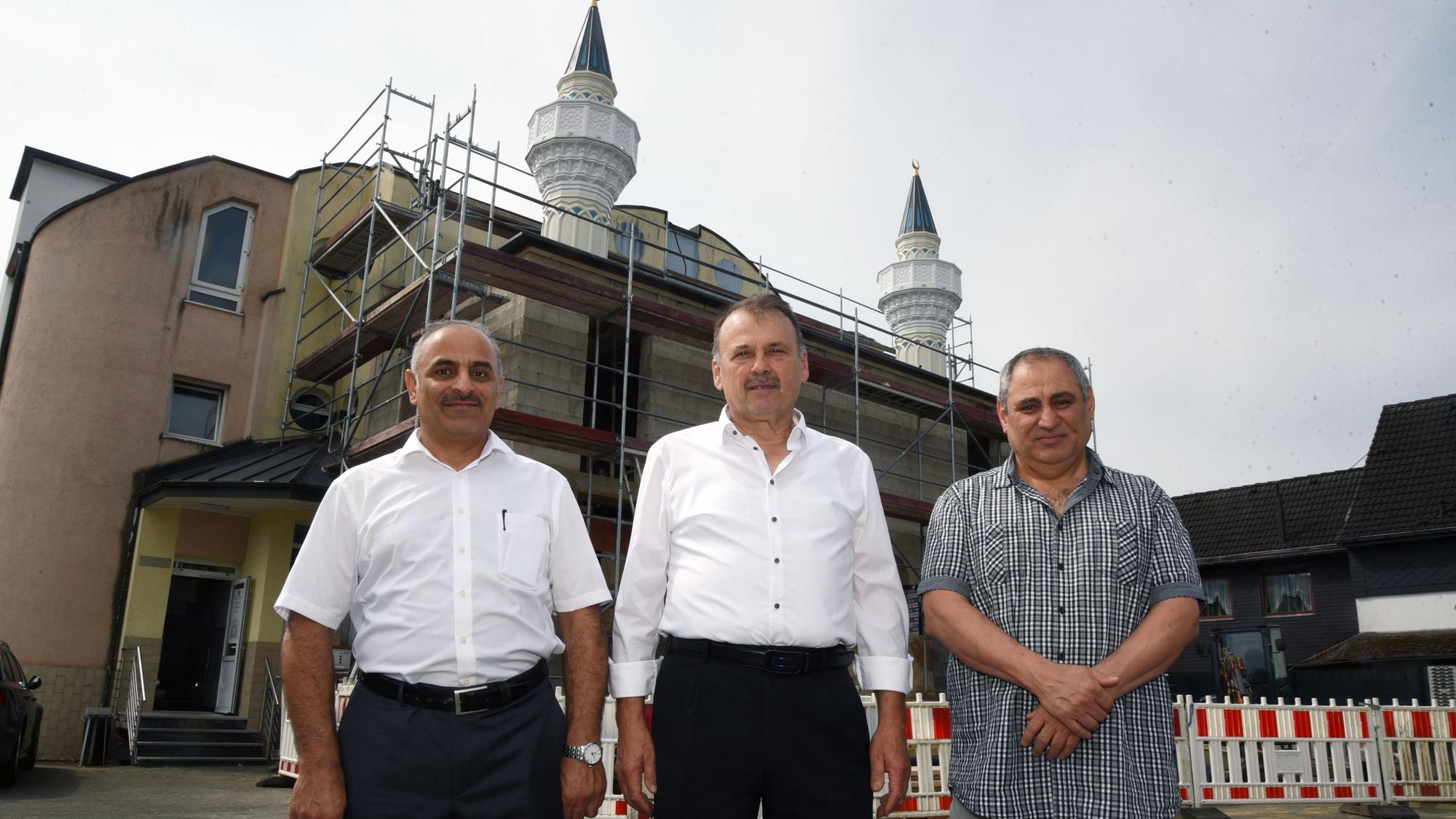 Drei Männer stehen vor einer Moschee, die sich gerade im Umbau befindet.