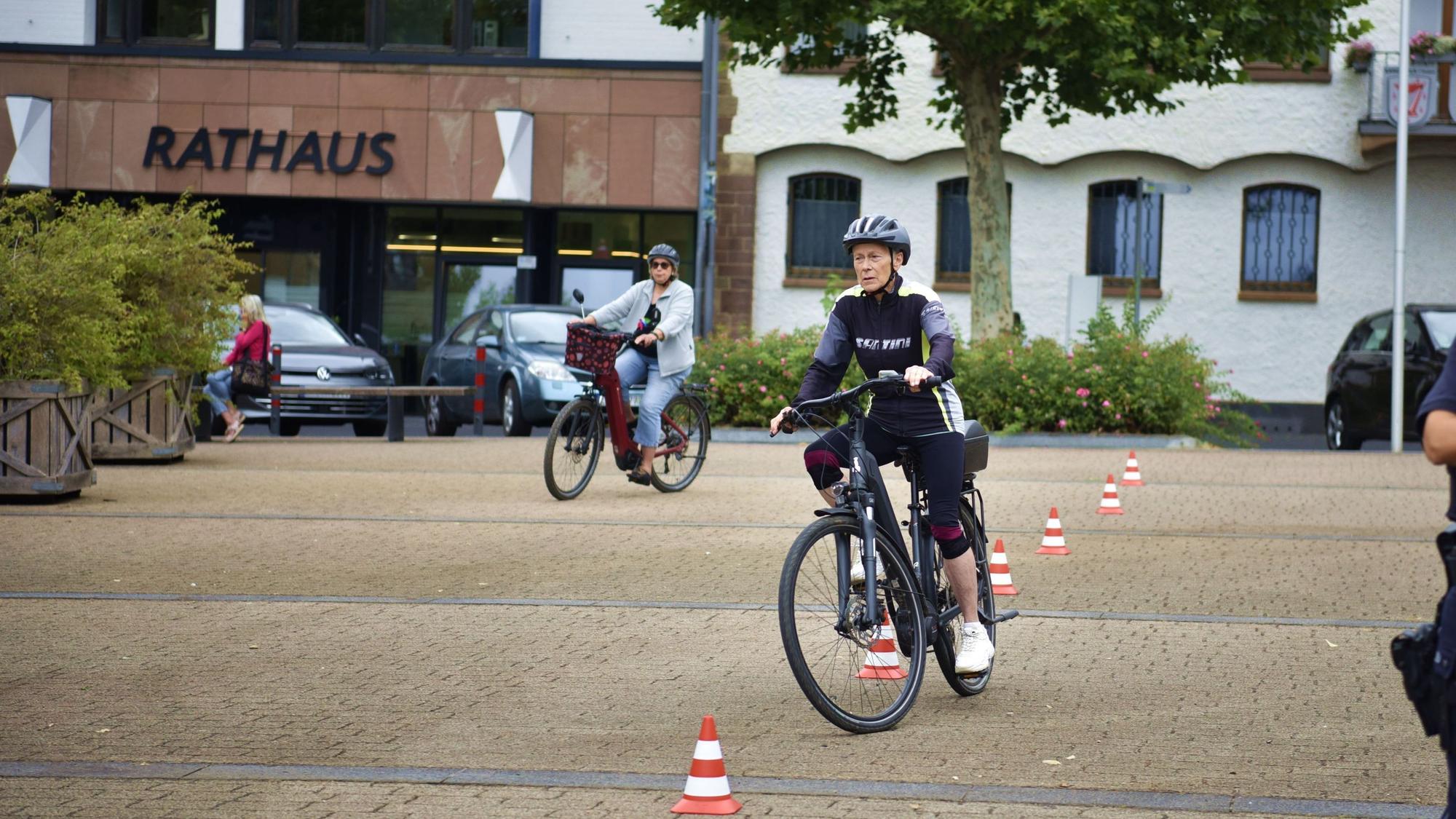 Eine Frau fährt mit einem Pedelc um rot-weiße Verkehrshütchen.