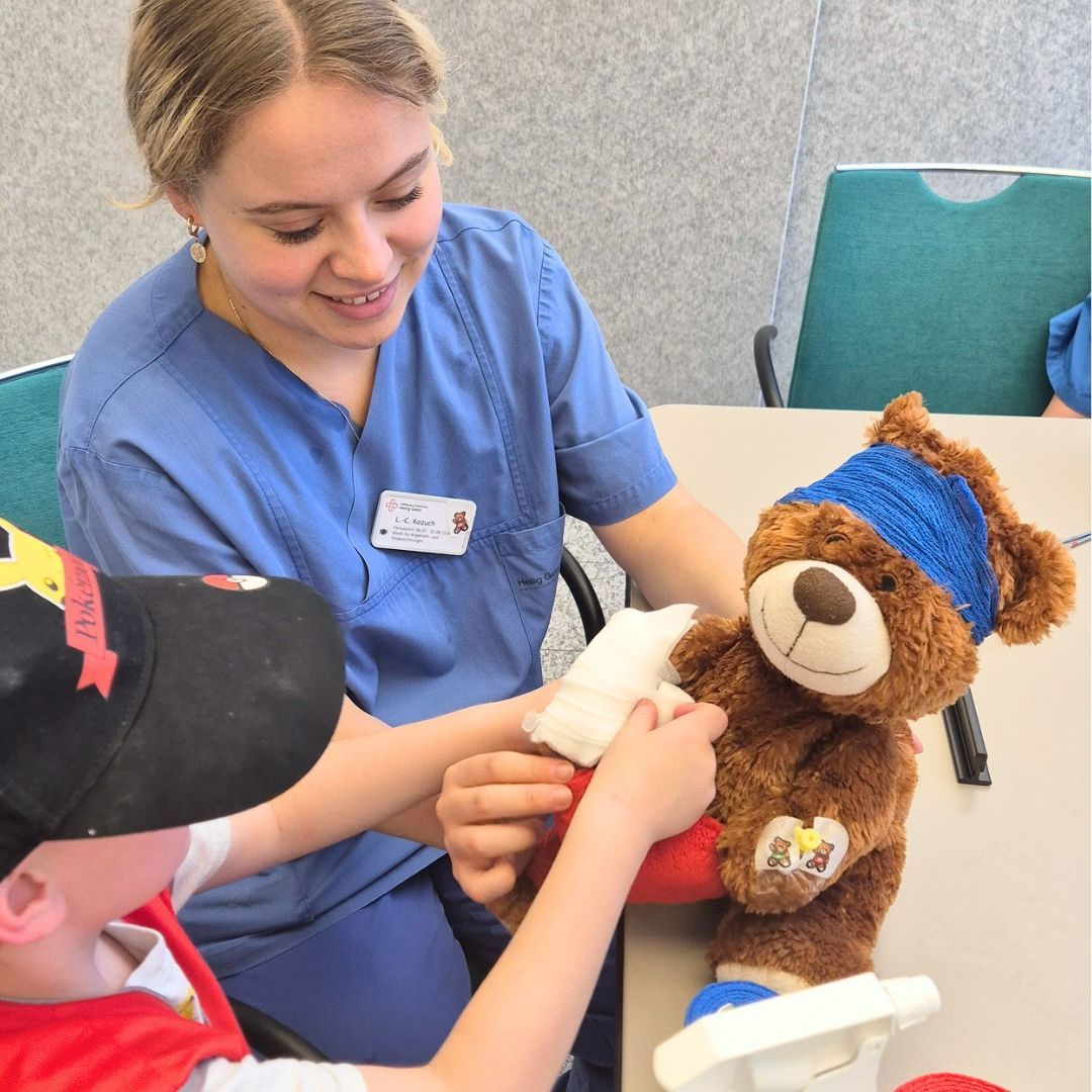 ein Teddybär wird von einem Kind und einer Krankenhausmitarbeiterin versorgt