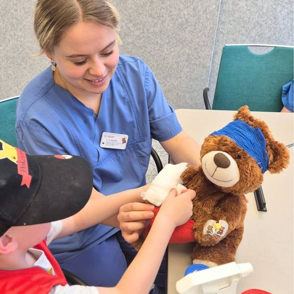 ein Teddybär wird von einem Kind und einer Krankenhausmitarbeiterin versorgt