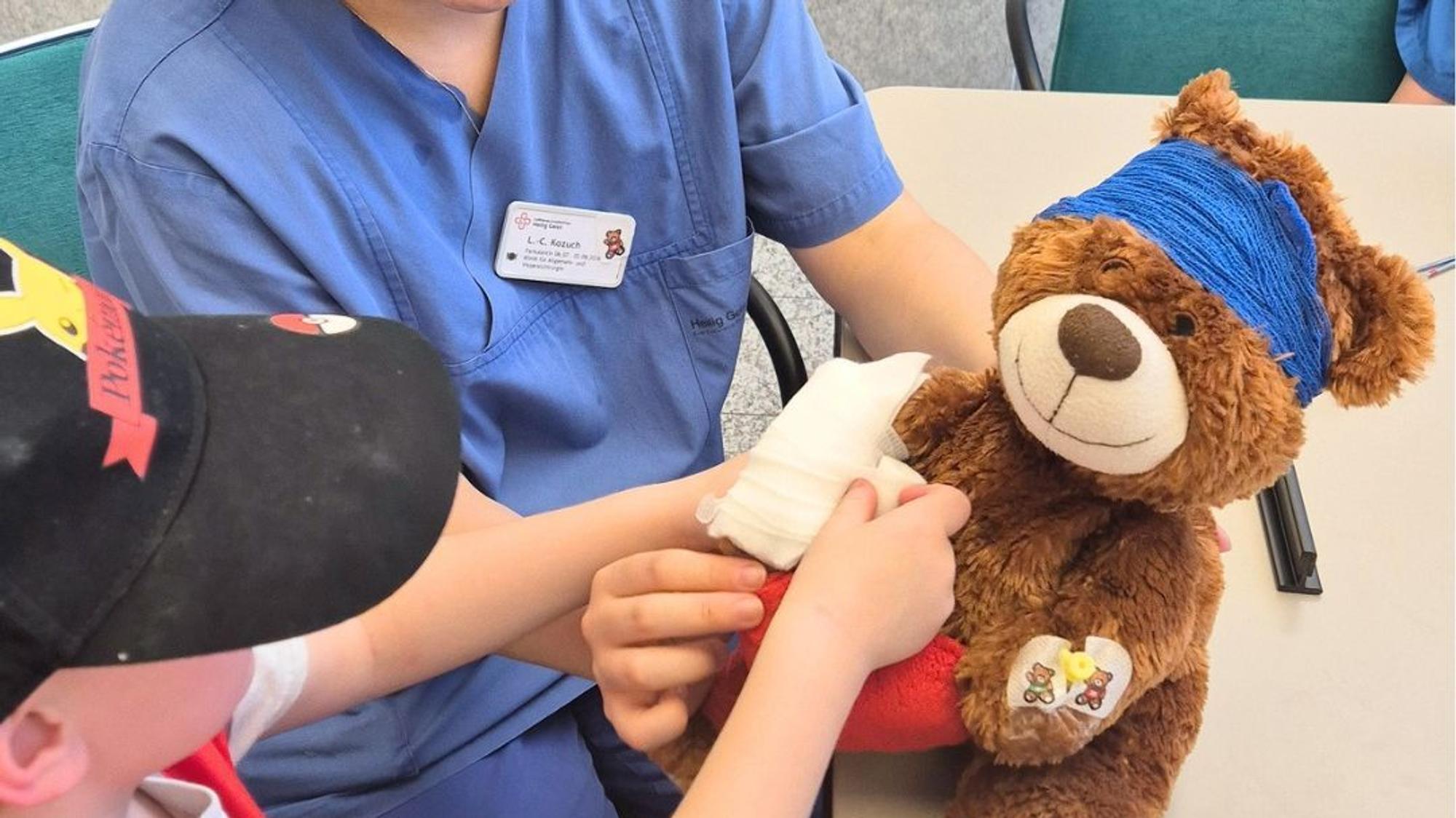 ein Teddybär wird von einem Kind und einer Krankenhausmitarbeiterin versorgt