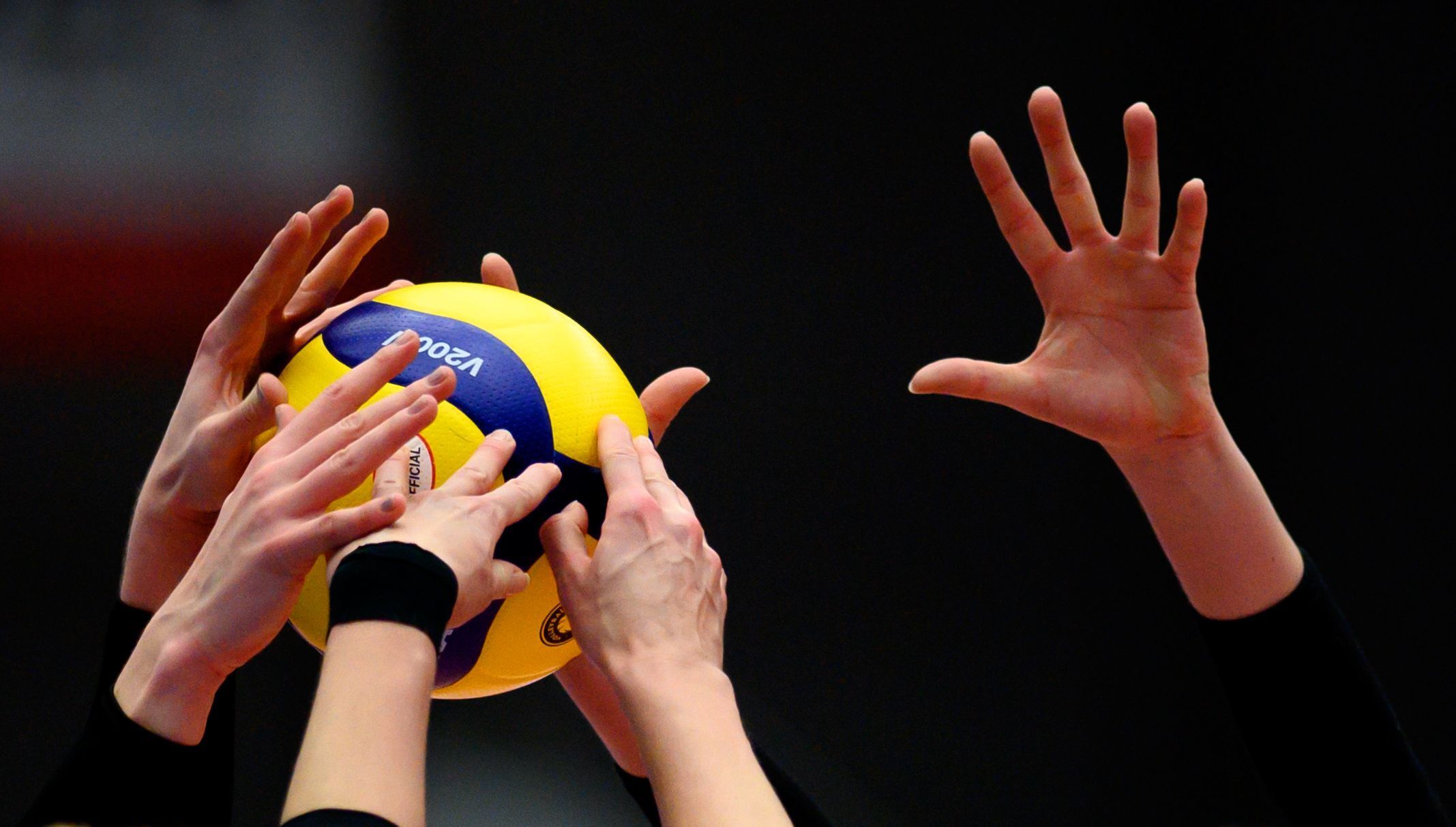 Mehrere Hände versuchen, an einen fliegenden Volleyball zu kommen.