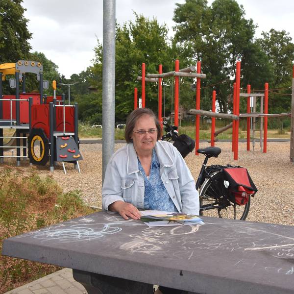 Das Foto zeigt eine Frau, die an einem Tisch vor einem Spielplatz sitzt.