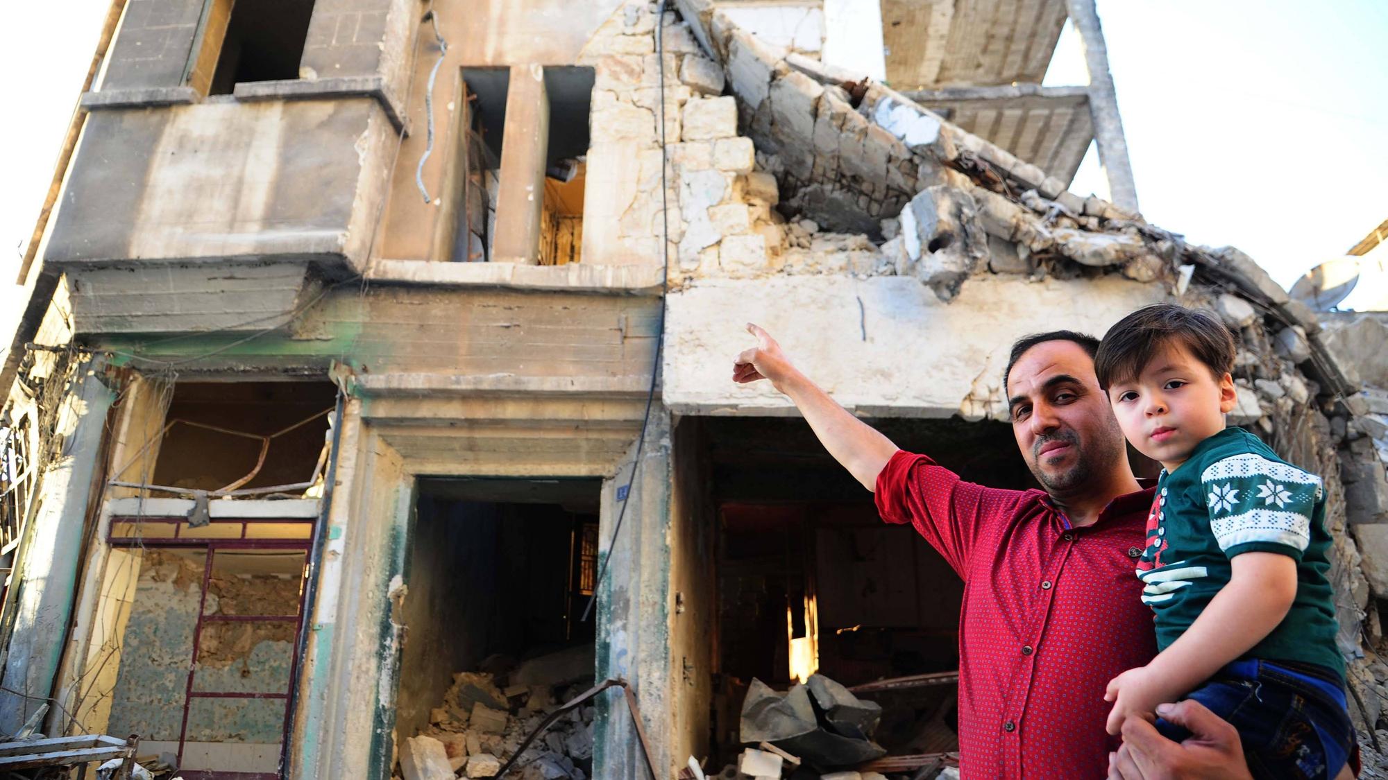 Omran Daqneesh (rechts) mit seinem Vater vor ihrem teilweise zerstörten Haus im Stadtteil Karm al-Qaterji in Aleppo. Das Foto entstand 2017, ein Jahr nachdem die Aufnahme des Jungen im Krankenwagen weltweit bekannt geworden war.