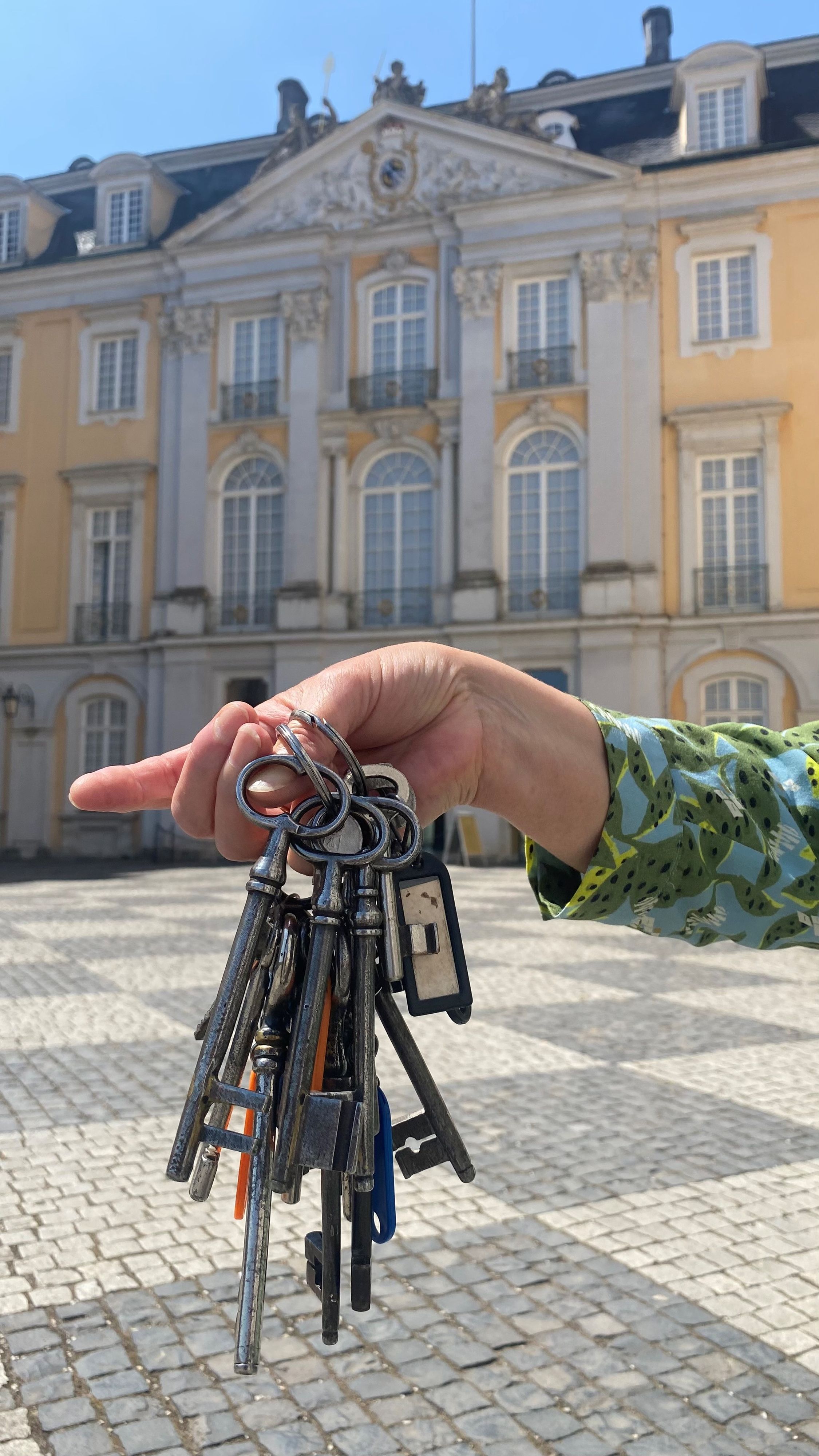 Zu sehen ist eine Hand, die ein Schlüsselbund hält. Im Hintergrund ist das Schloss Augustusburg zu sehen.