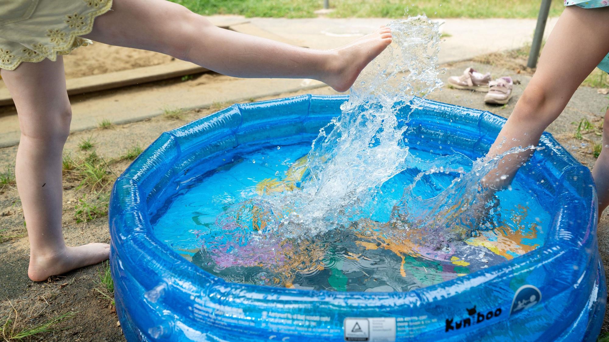 Kinder spielen in einer Kindertagesstätte in einem Planschbecken. Auf dem Symbolbild sind die Füße und Beine von zwei Kindern zu sehen.
