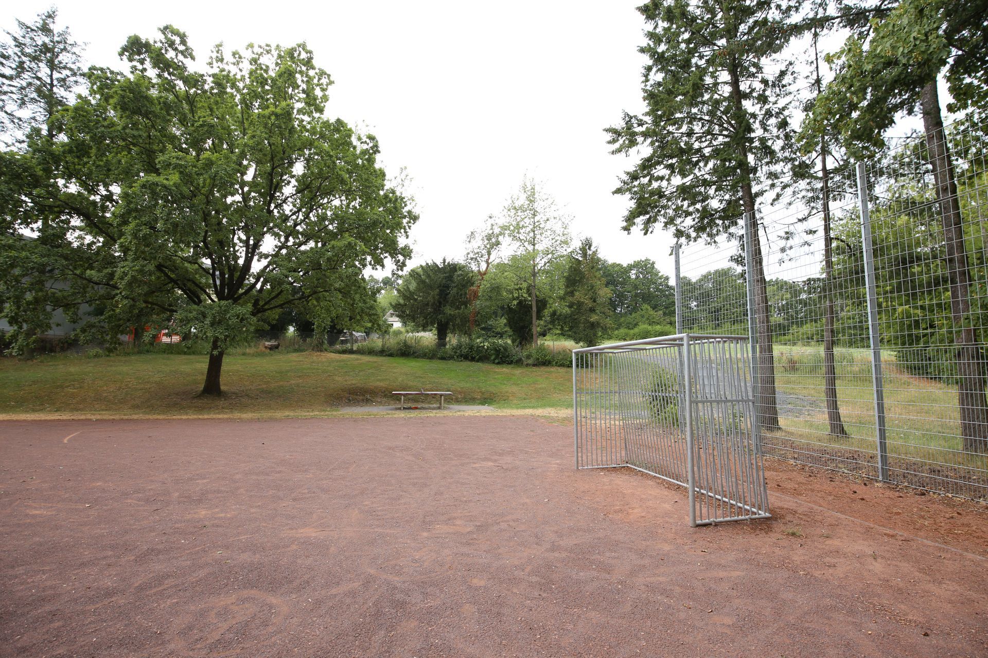 Ein kleiner Bolzplatz mit einem Fußballtor, im Hintergrund Wiesen und Bäume.