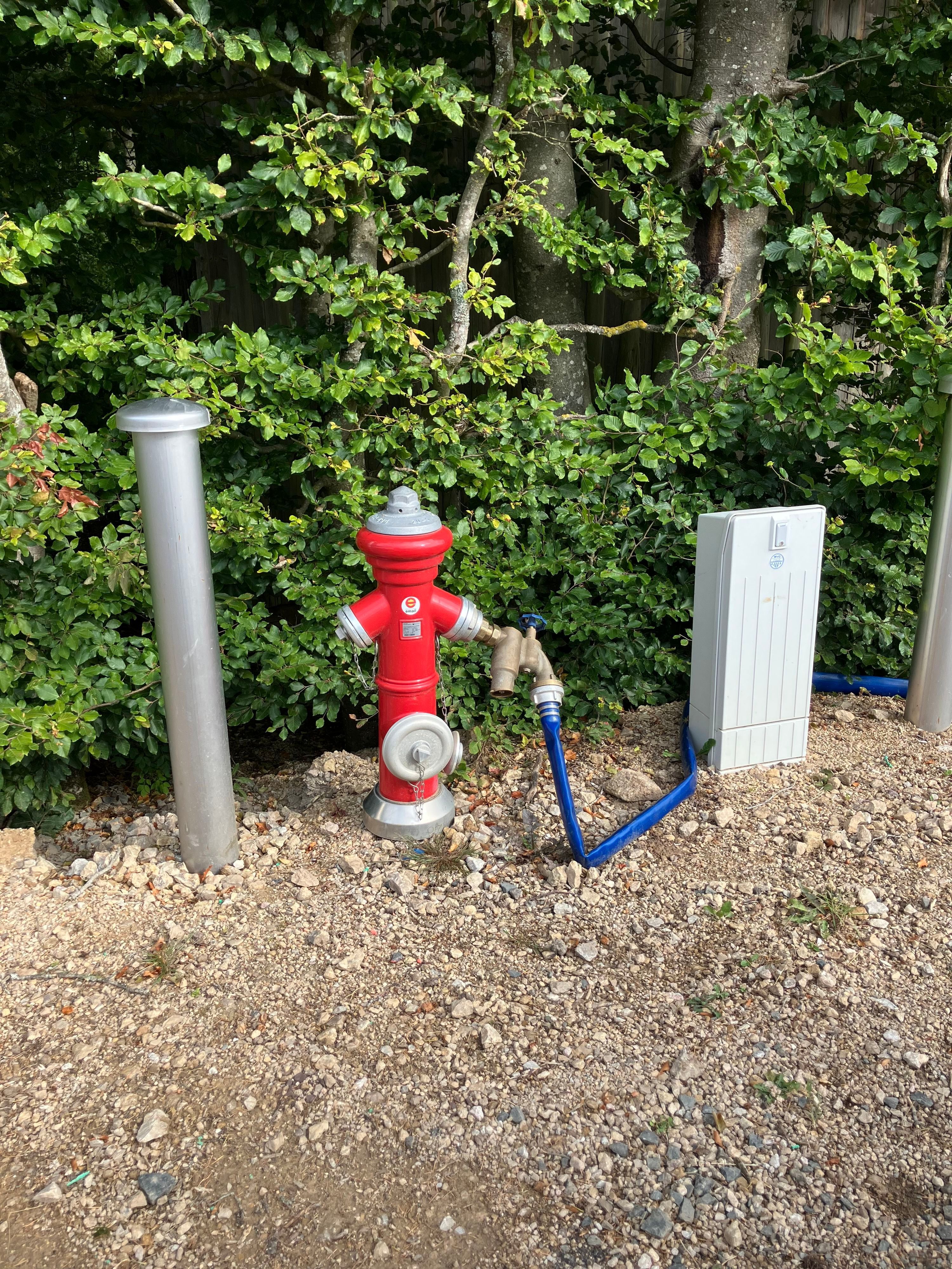 Das Bild zeigt einen roten Hydranten, an den ein blauer Wasserschlauch angeschlossen ist.