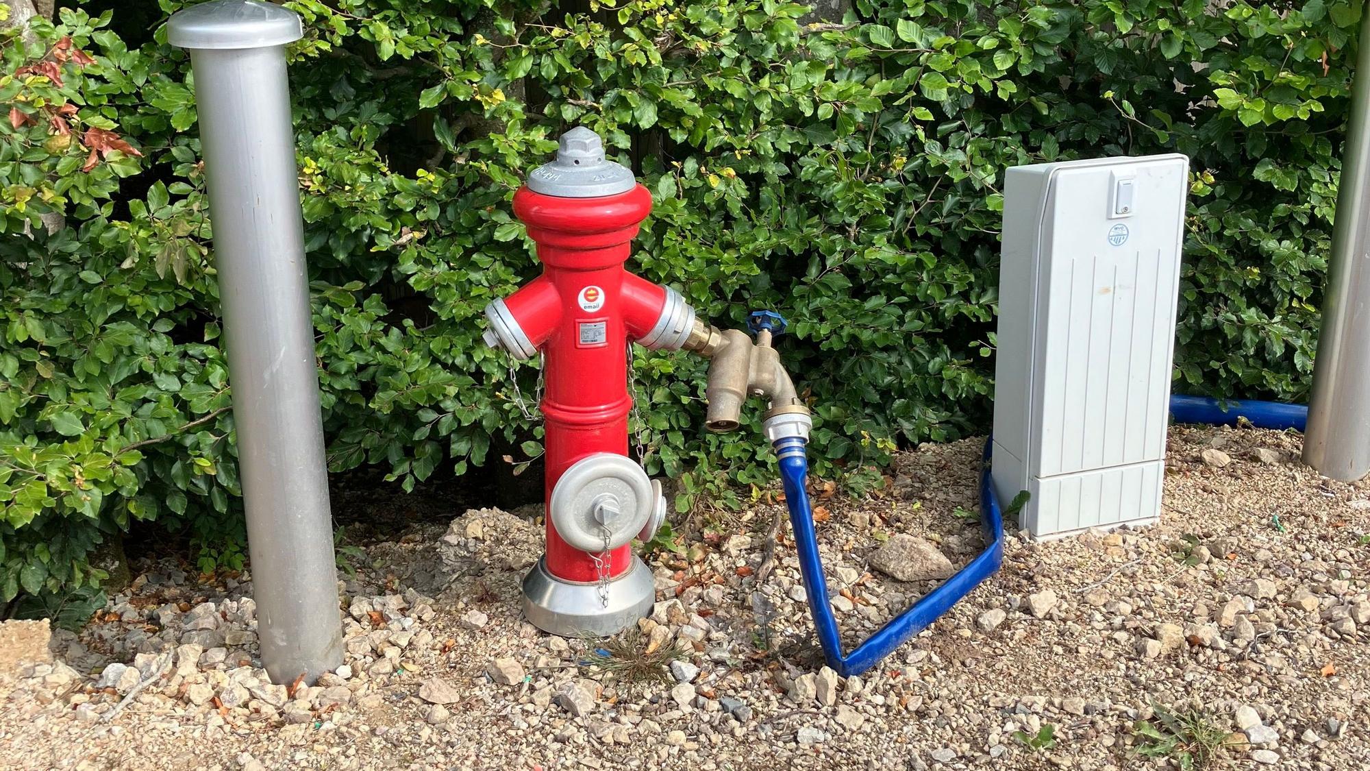 Das Bild zeigt einen roten Hydranten, an den ein blauer Wasserschlauch angeschlossen ist.