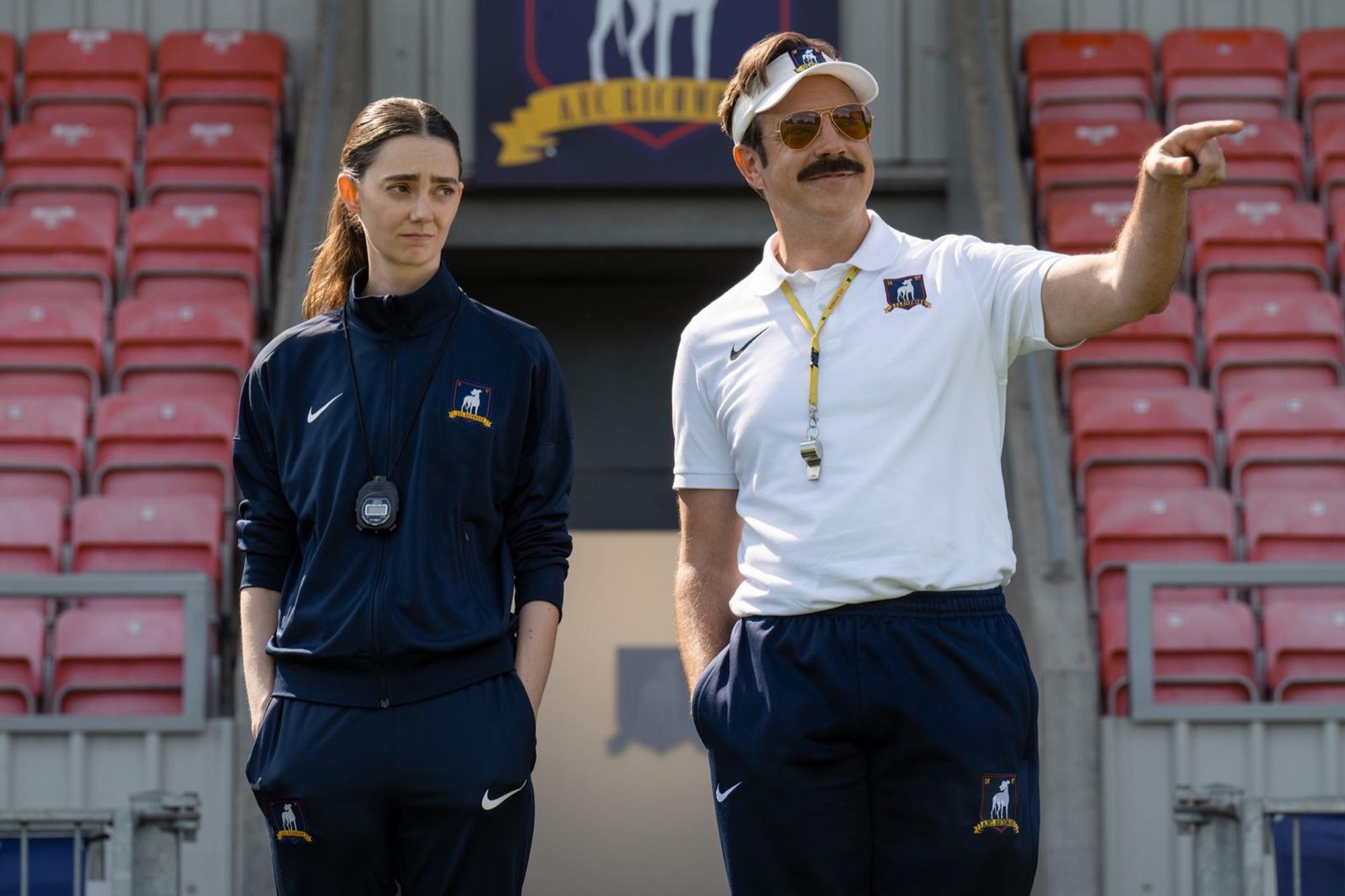 Ted Lasso (Jason Sudeikis) ist zurück: Dass ausgerechnet ein Mann die Lady Greyhounds trainiert, findet Alice Chilton(Tanya Reynolds) allerdings nicht so prickelnd. (Bild: © Apple TV / Collin Hutton)
