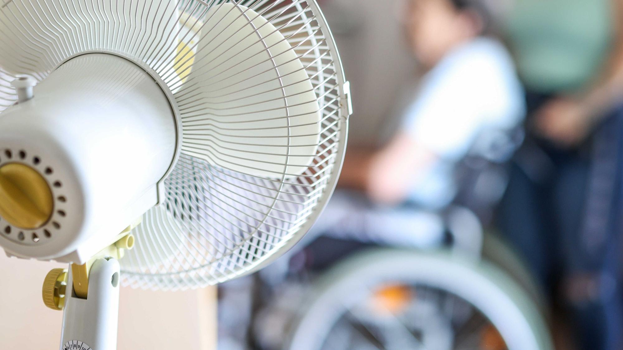 Ein Ventilator steht in einem Aufenthaltsraum eines Seniorenheims, davor sitzt eine Seniorin in einem Rollstuhl. (Symbolbild)