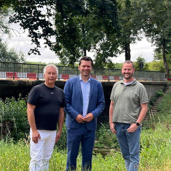 Das Fotos zeigt drei Männer vor einer Brücke.
