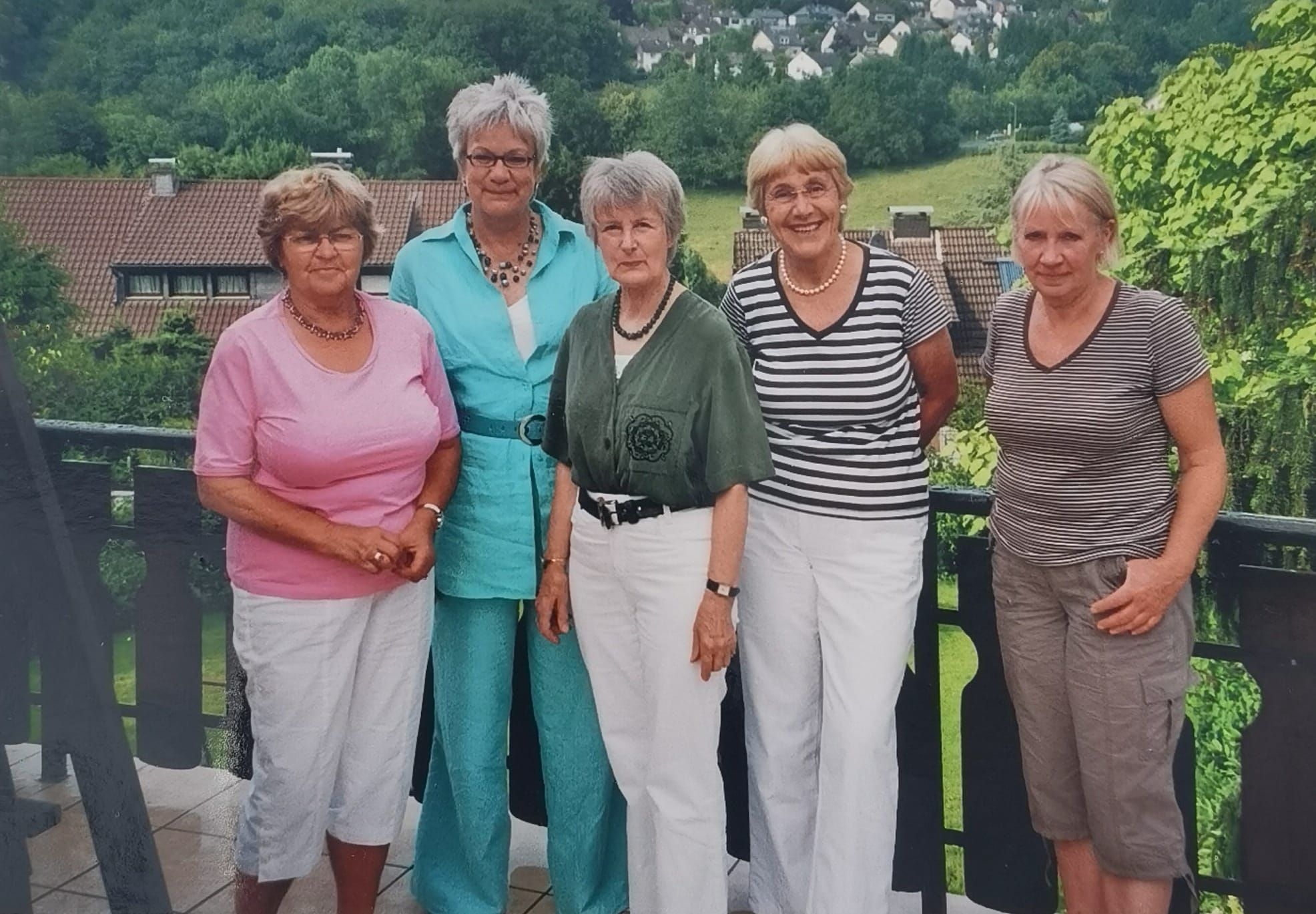 Fünf Frauen stehen auf einem Balkon nebeneinander und lächeln.