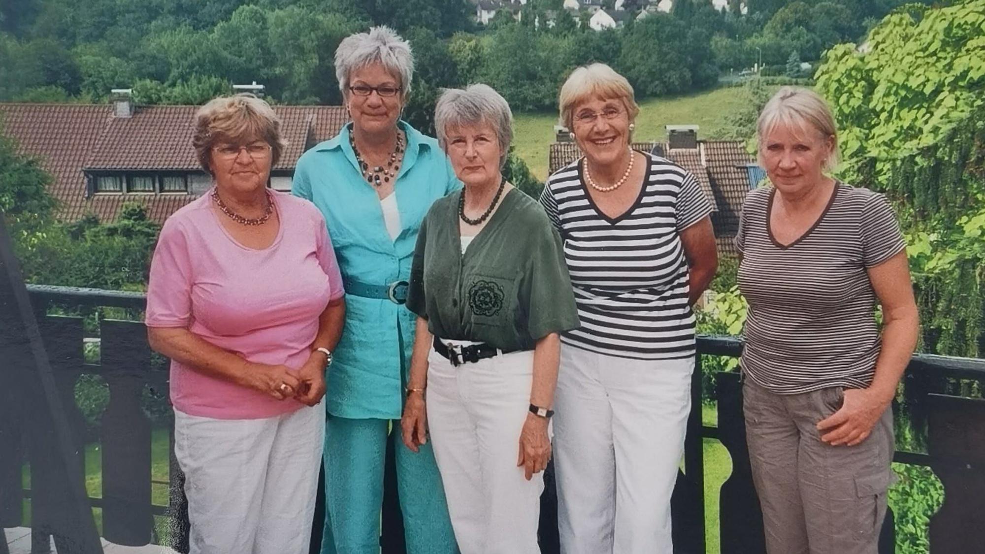 Fünf Frauen stehen auf einem Balkon nebeneinander und lächeln.
