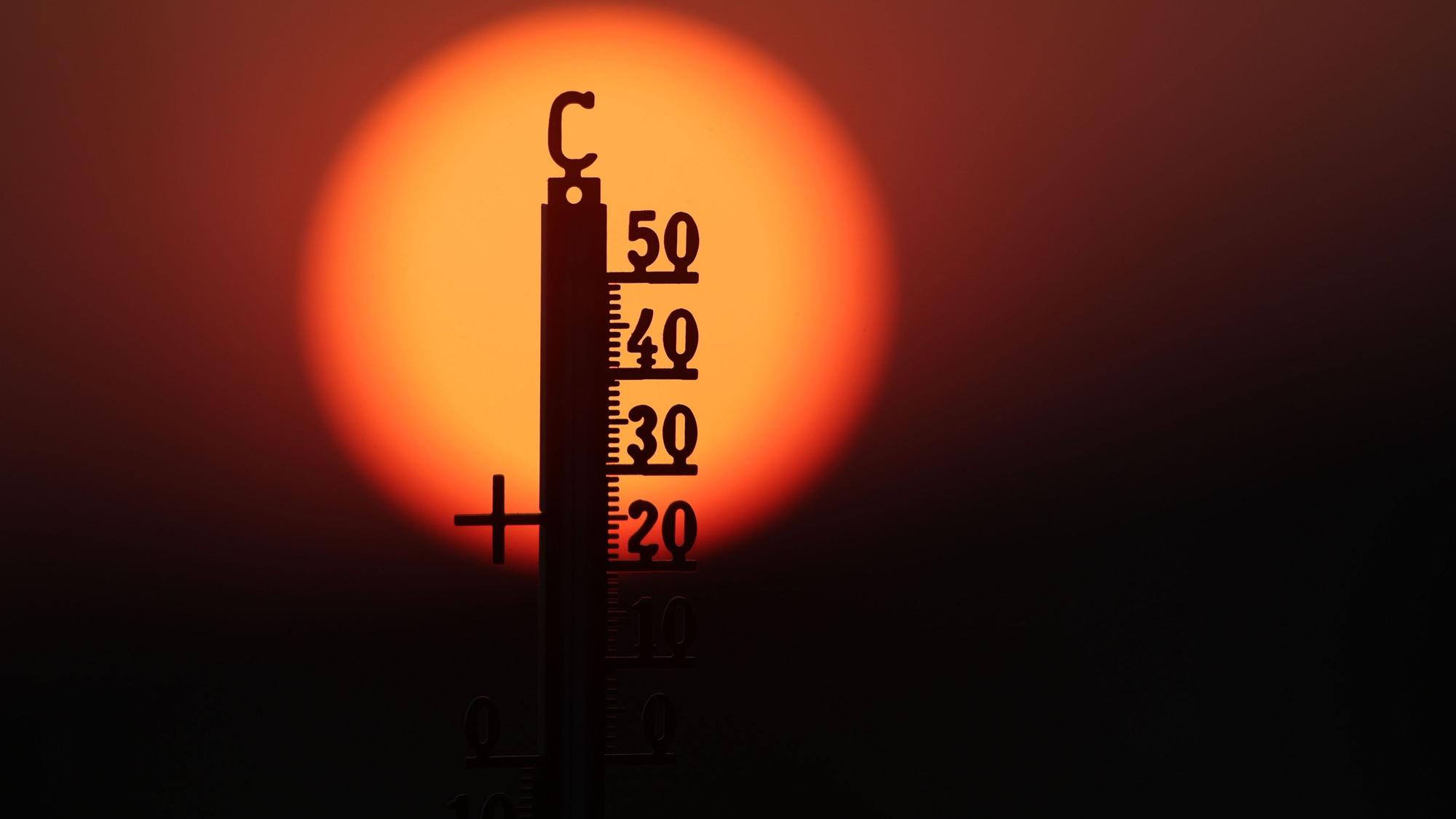 Hinter einem Thermometer geht am Morgen die Sonne auf. (Symbolbild)