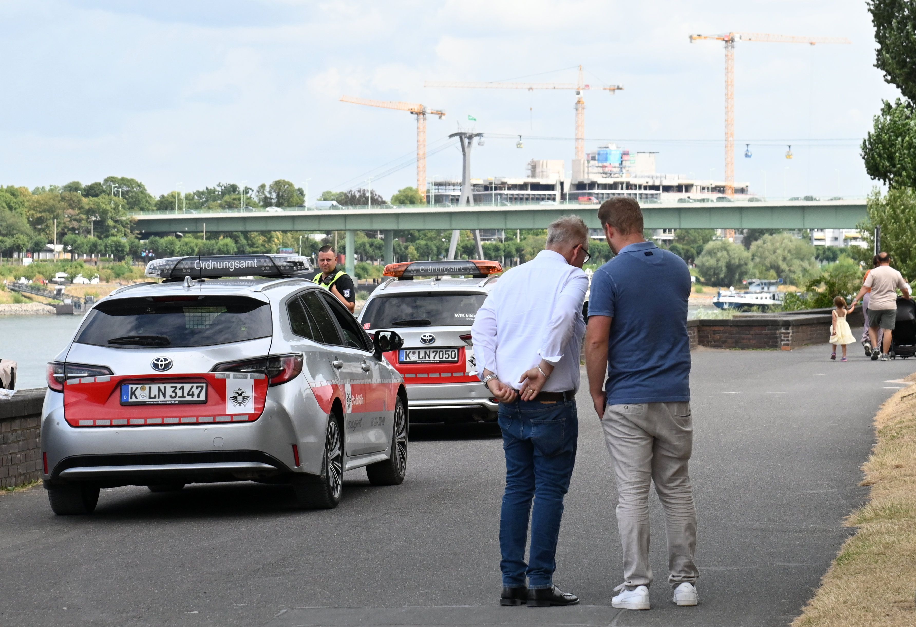 Zwei Männer stehen mit dem Rücken zur Kamera. Daneben ein Auto vom Ordnungsamt.