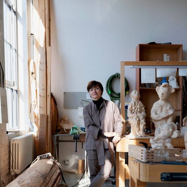 Eine Frau steht in einem Atelier, in Regalen befinden sich mehrere Skulpturen.