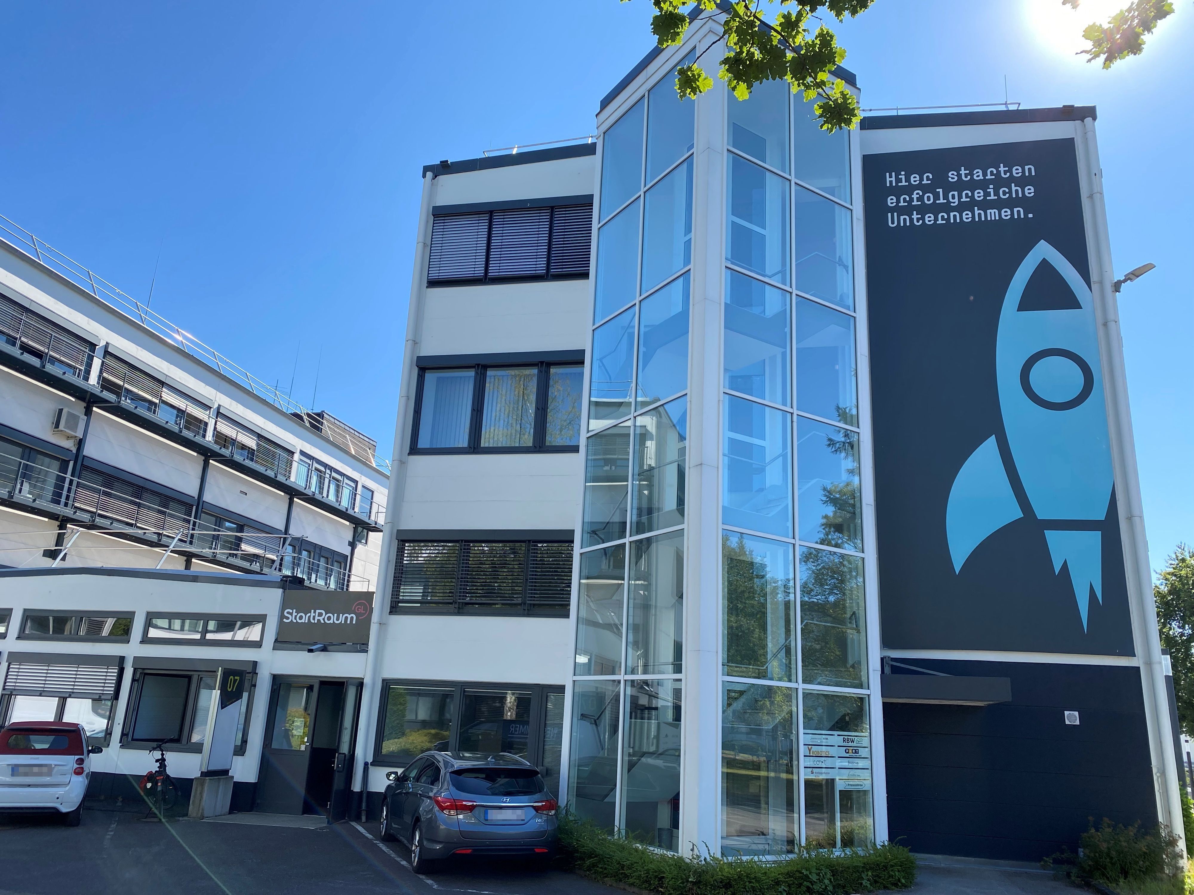 ein dreistöckiges Bürohaus mit einer Raketen-Grafik an der Fassade, daneben ein Flachbau mit dem Schriftzug "Startraum"