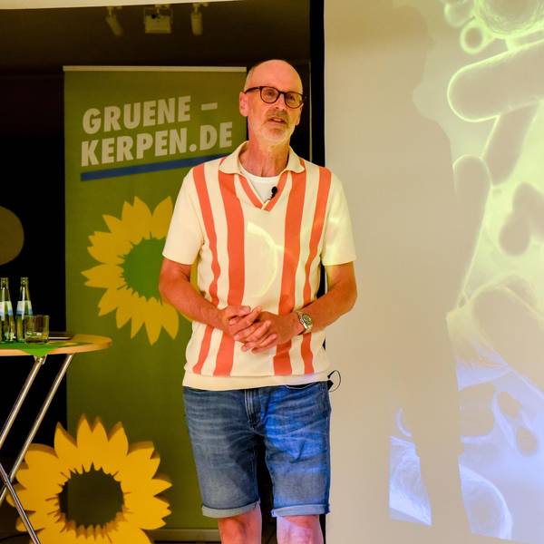 Ein Mann steht neben einem Tisch, er hält einen Vortrag.