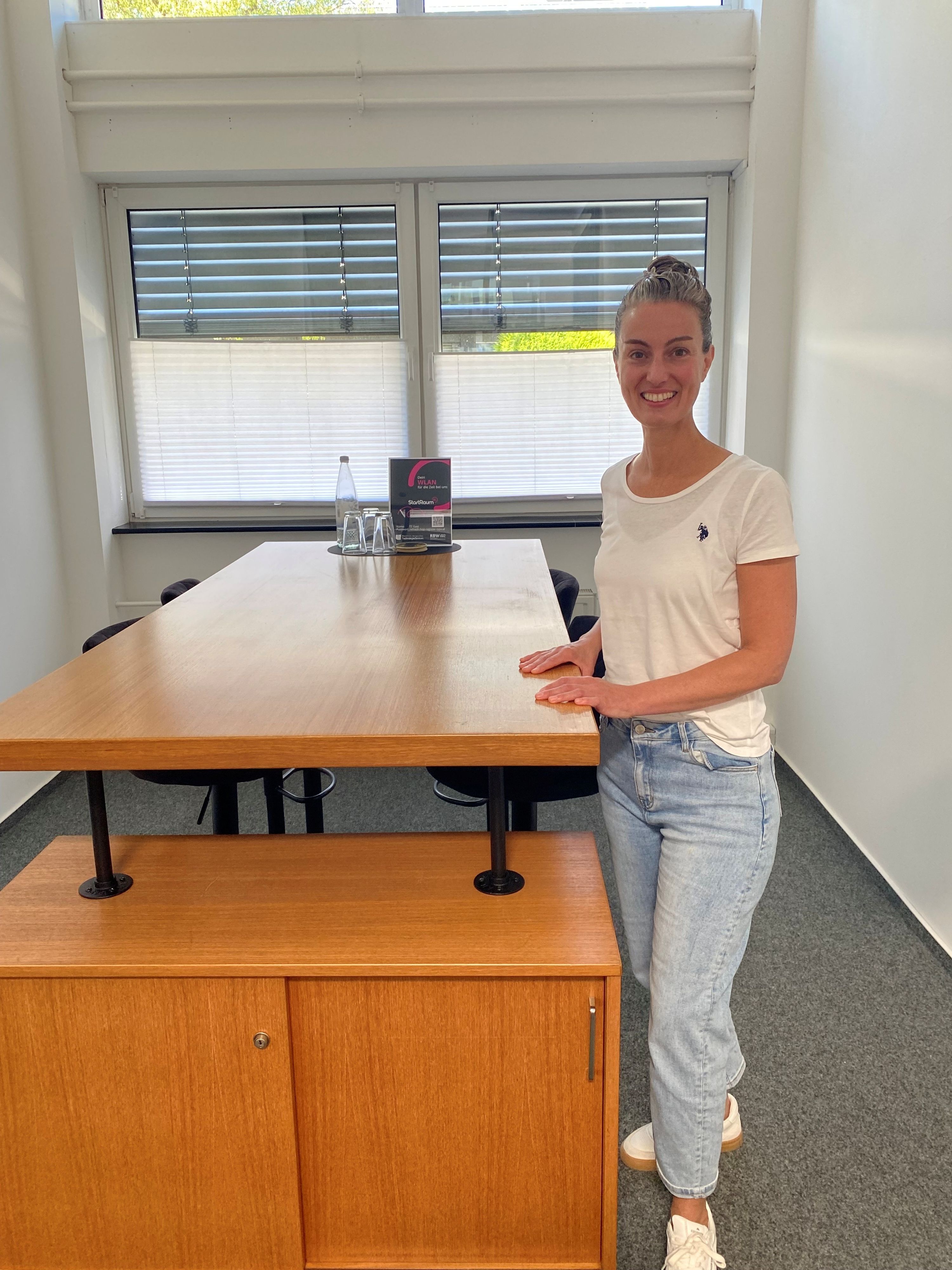 eine junge Frau steht an einem Hochtisch mit brauner Tischplatte und lächelt