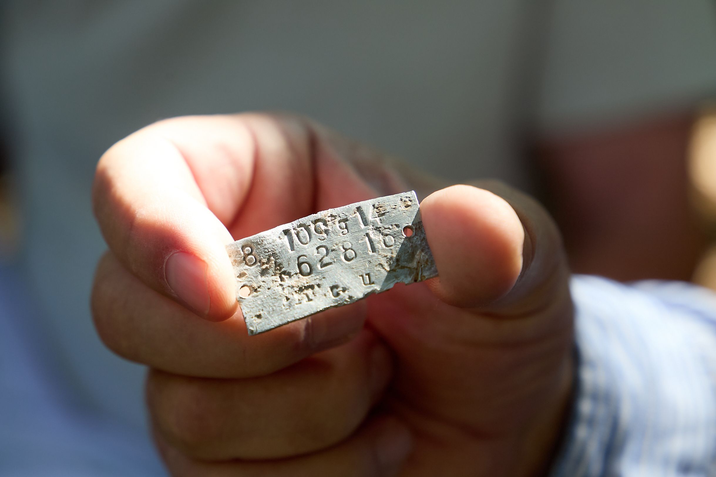 Ein Mann hällt ein Metallplättchen, auf dem Zahlen stehen, zwischen Daumen und Zeigefinger.