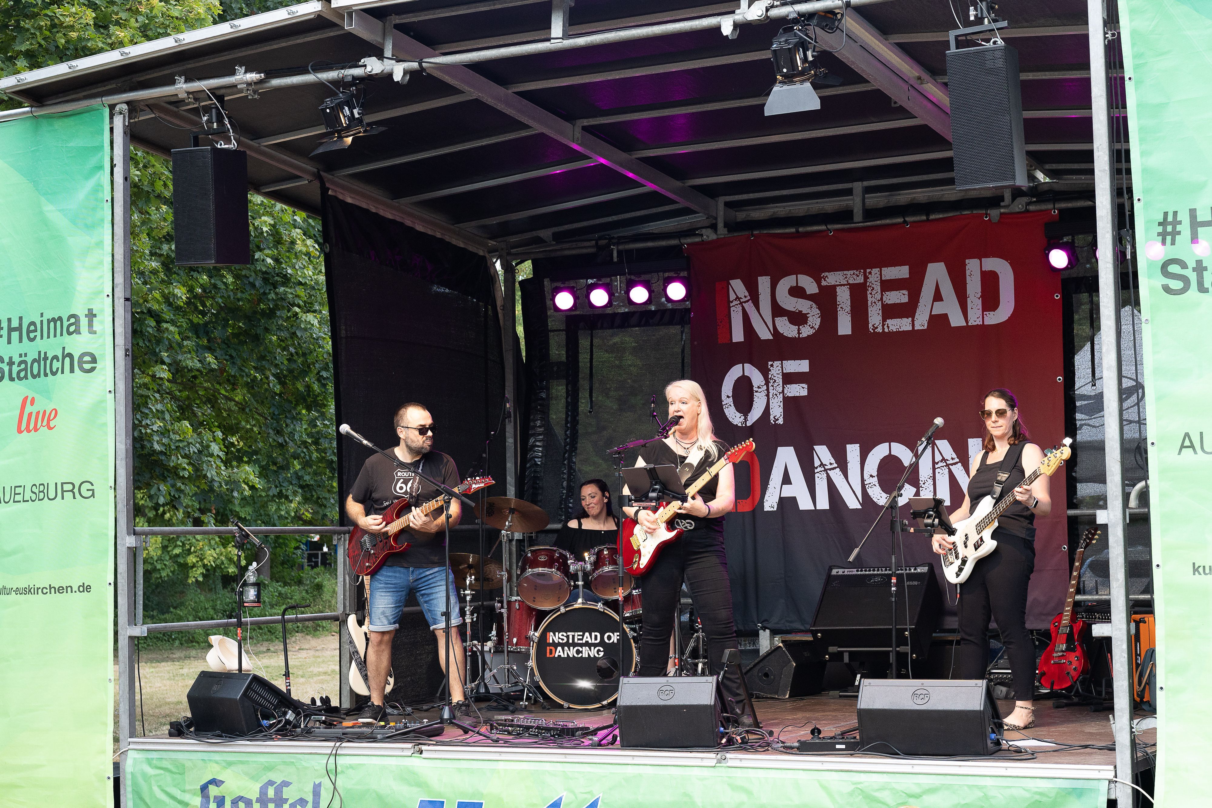Ein Gitarrist, die Sängerin, die ebenfalls Gitarre spielt, und eine Bassistin stehen vorne auf der Bühne, im Hintergrund ist die Schlagzeugerin zu sehen.