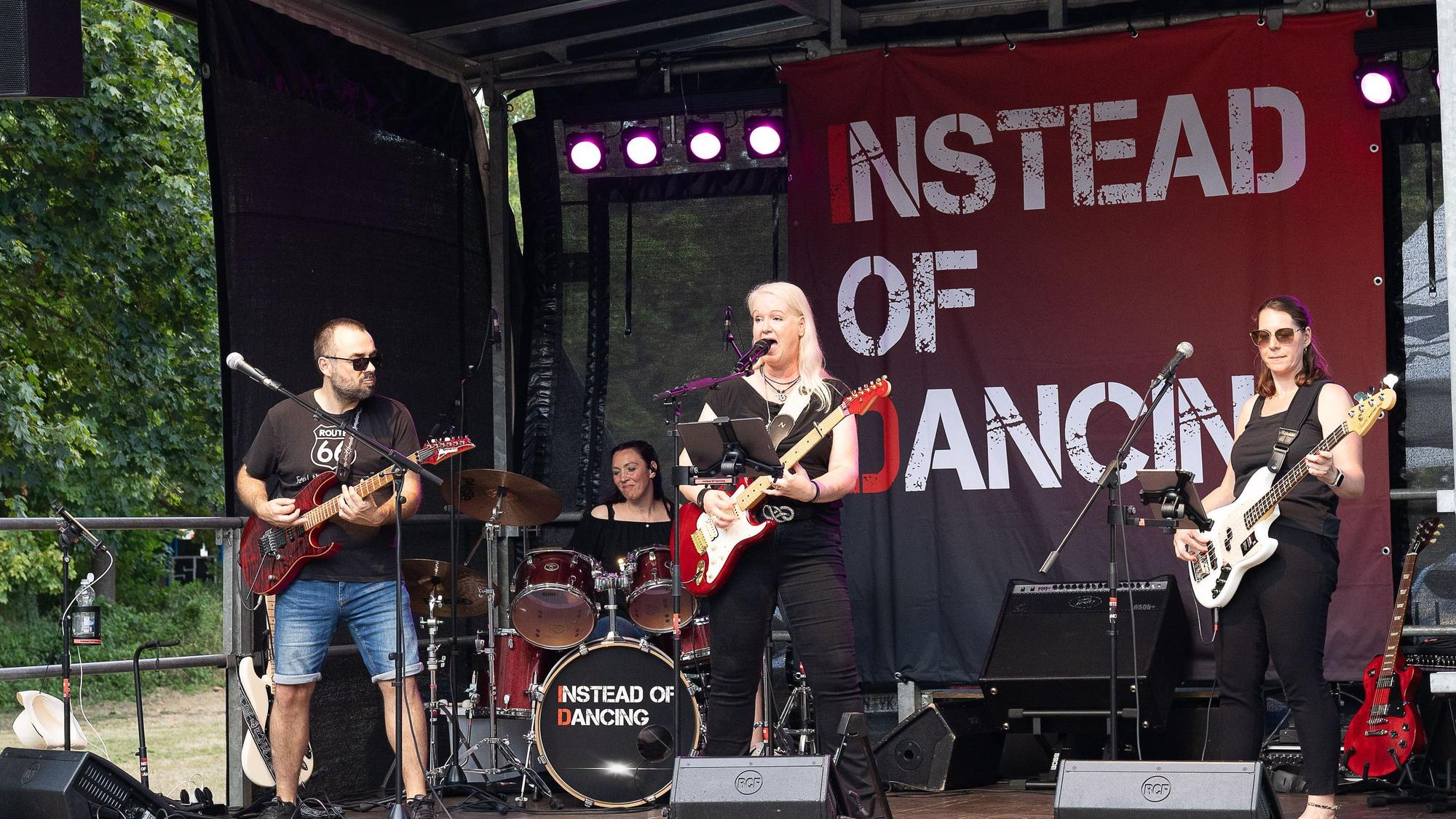 Ein Gitarrist, die Sängerin, die ebenfalls Gitarre spielt, und eine Bassistin stehen vorne auf der Bühne, im Hintergrund ist die Schlagzeugerin zu sehen.