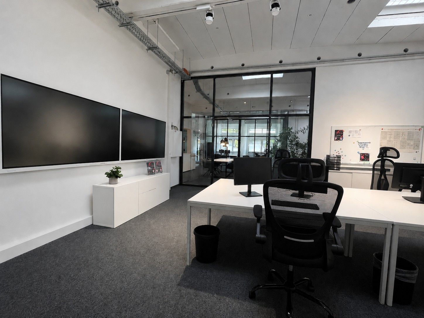 Ein Büroraum mit großen Monitoren und Glastüren