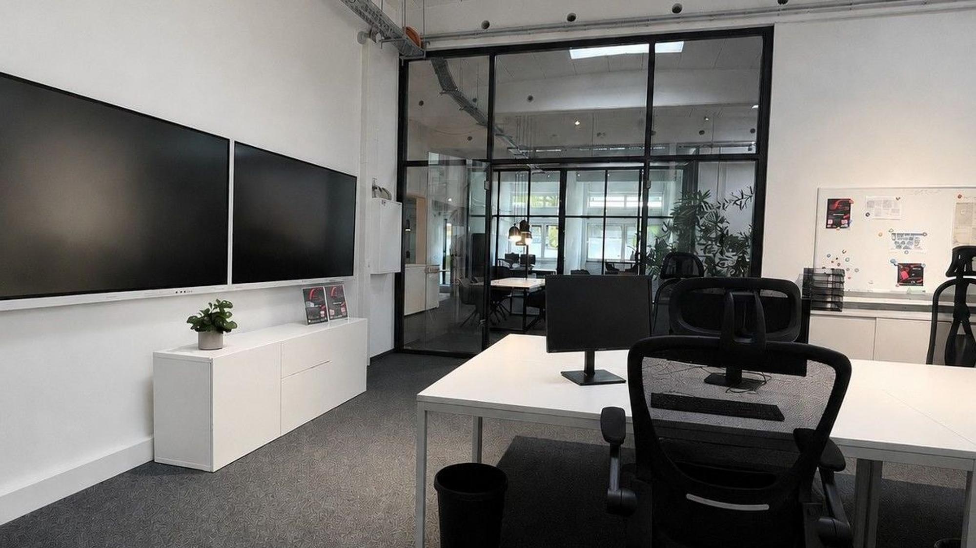 Ein Büroraum mit großen Monitoren und Glastüren