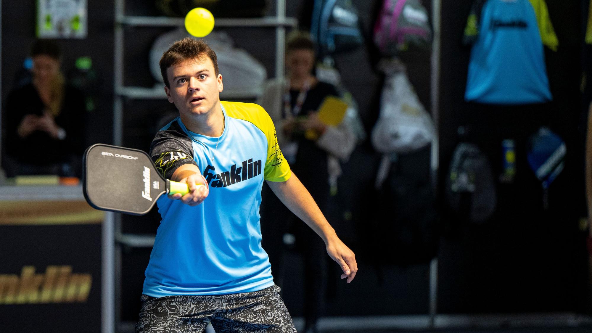 Ein junger Mann schlägt mit einem Pickleball-Schläger nach einem gelben Ball.