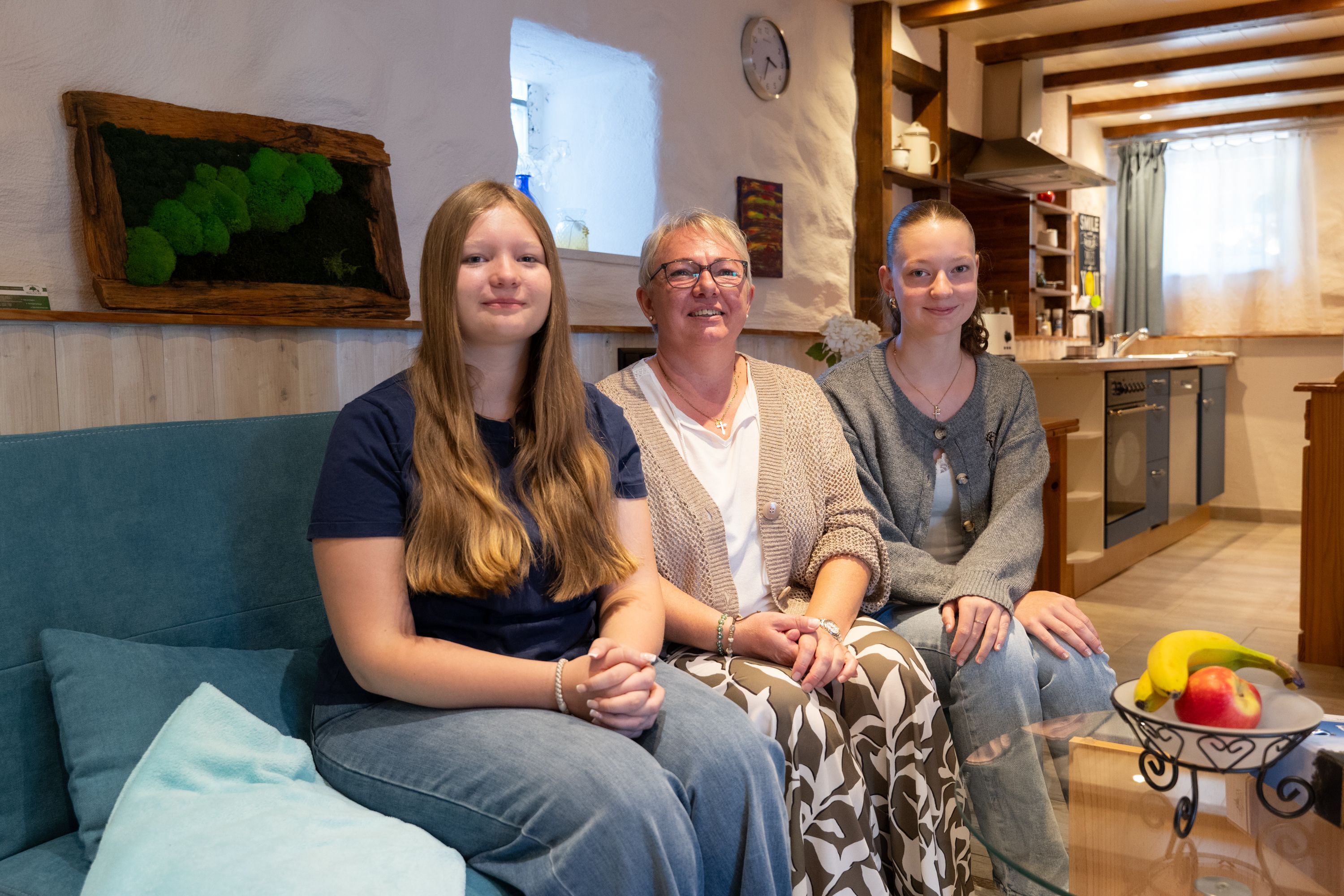 Eine Mutter sitzt mit ihren beiden Töchtern in einer Ferienwohnung auf einem Sofa.