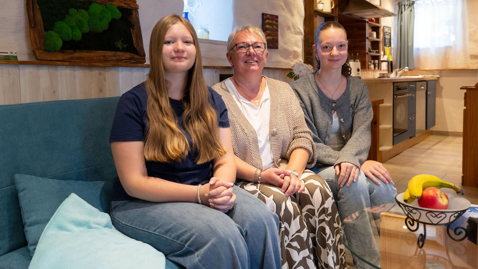 Eine Mutter sitzt mit ihren beiden Töchtern in einer Ferienwohnung auf einem Sofa.