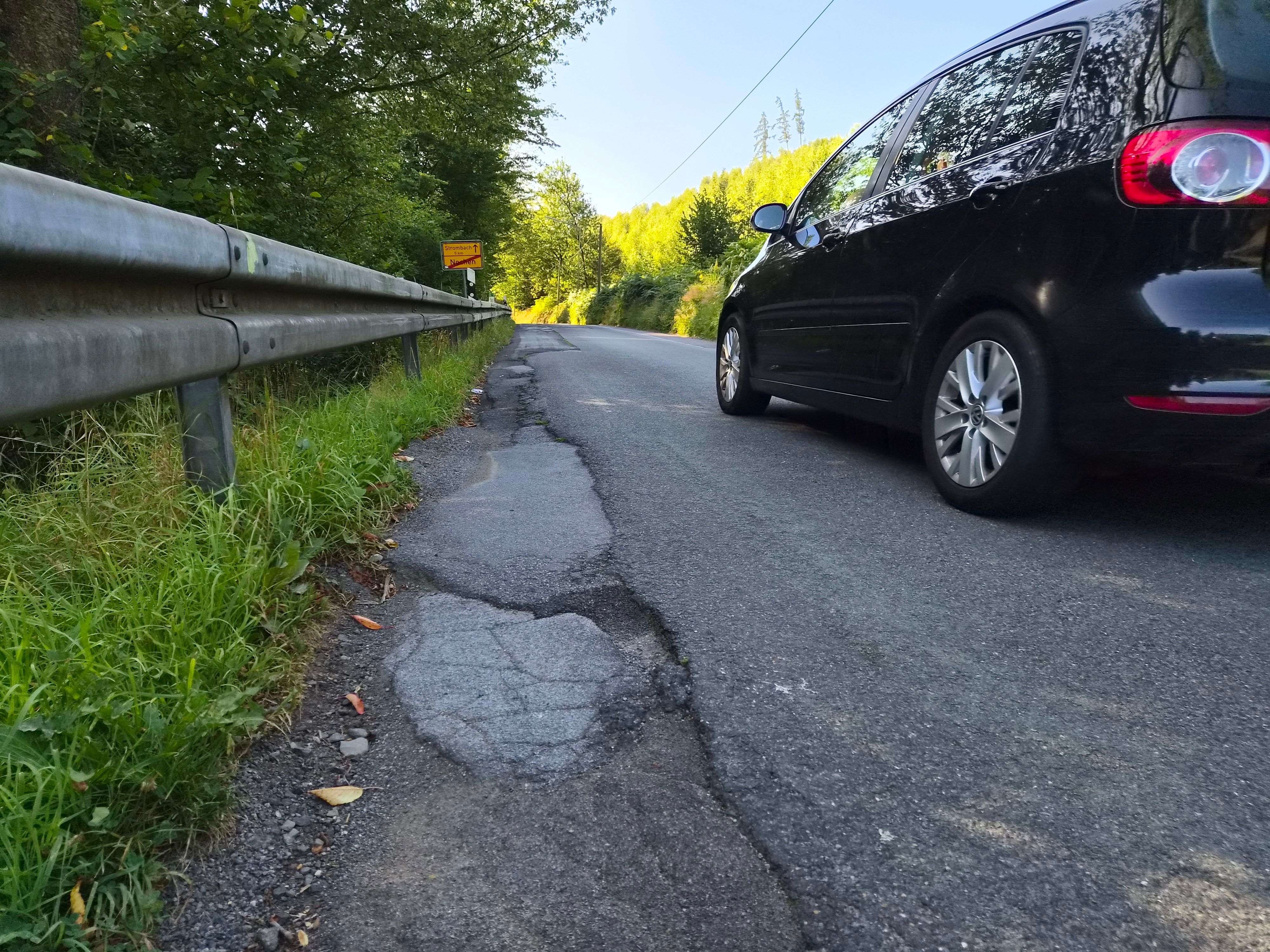 Ein Auto neben kaputtem Asphalt.