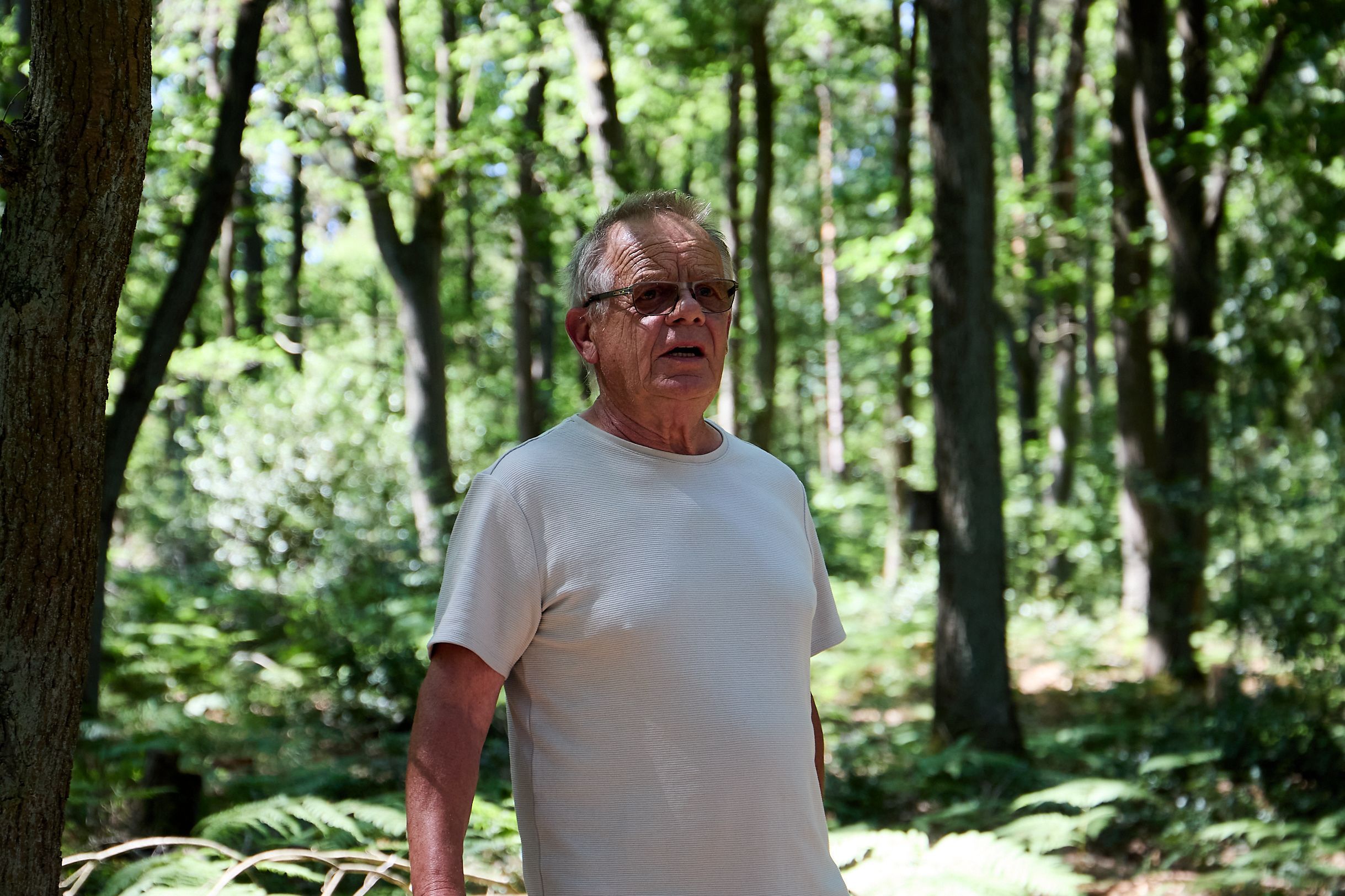 Ein Mann mit Sonnenbrille steht im T-Shirt im Wald.