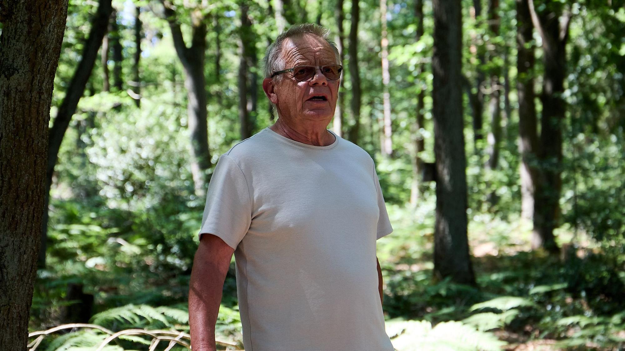 Ein Mann mit Sonnenbrille steht im T-Shirt im Wald.