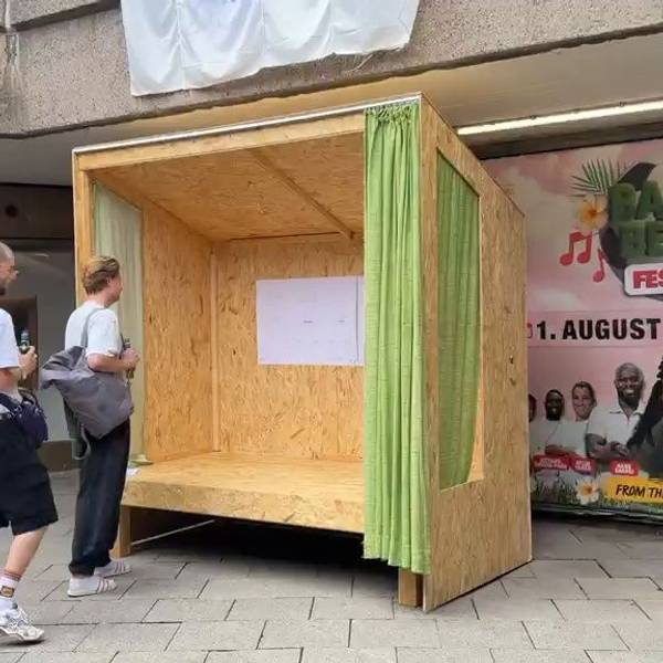 Zwei Männer stehen vor einer überdachten Holzbank.